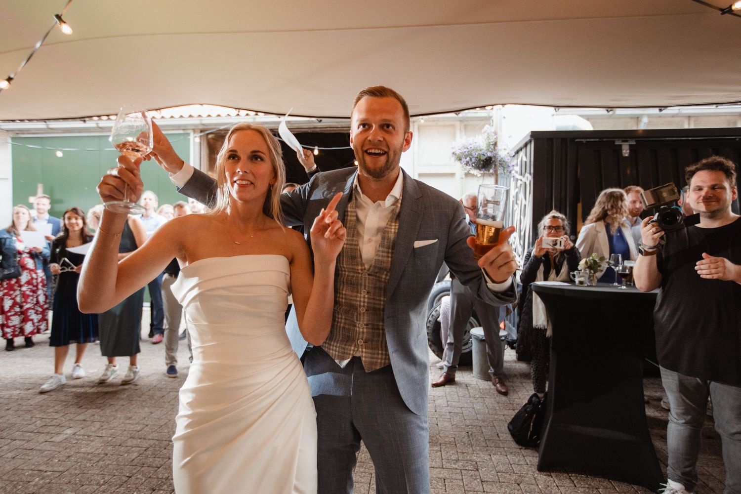 Lively wedding reception with guests dancing in rows under tent lighting.
