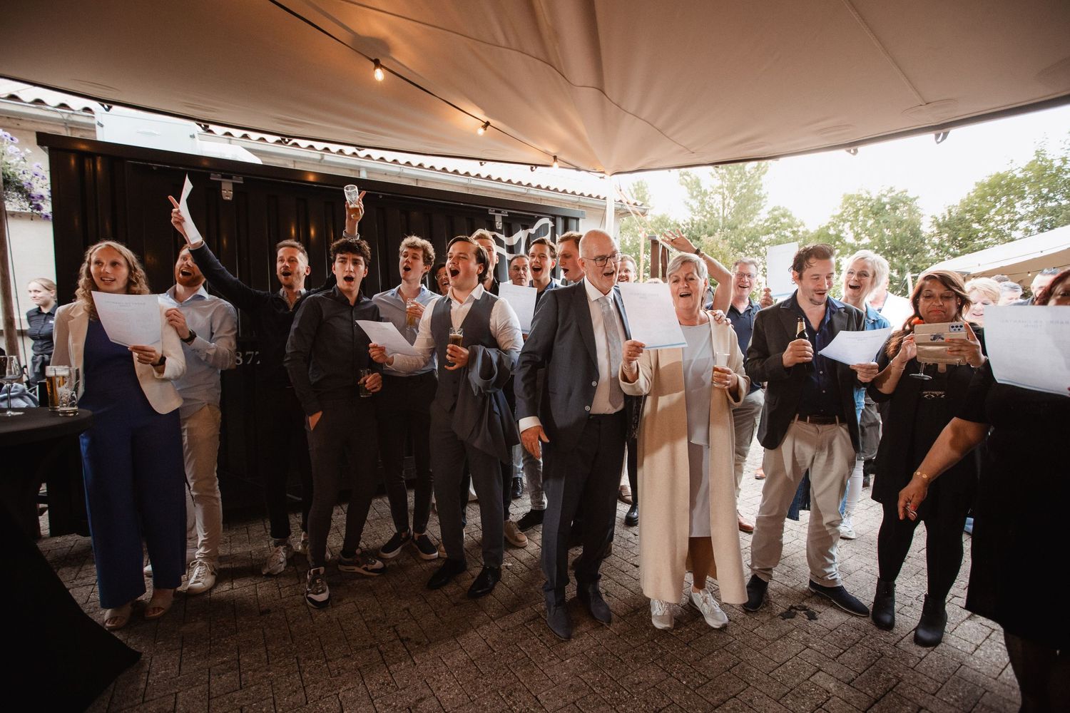 Wide shot of wedding celebration showing guests dancing and mingling under large outdoor tent.