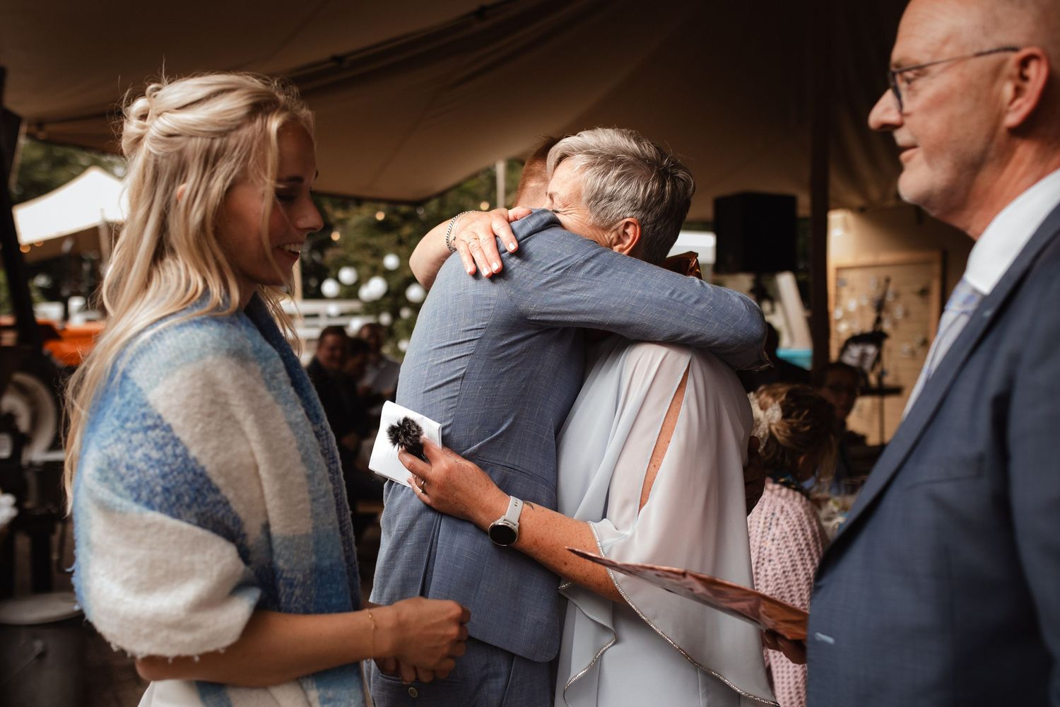 Emotional embrace between guests at outdoor celebration under tent.