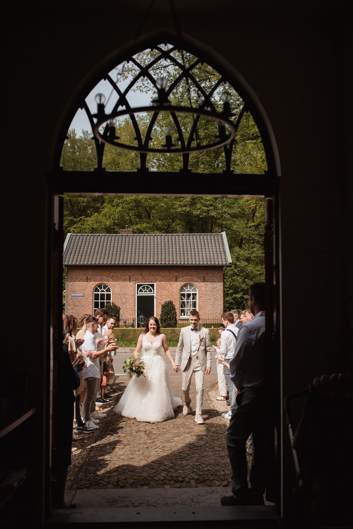 A wedding ceremony viewed through an arched doorway of a brick church on a sunny day.