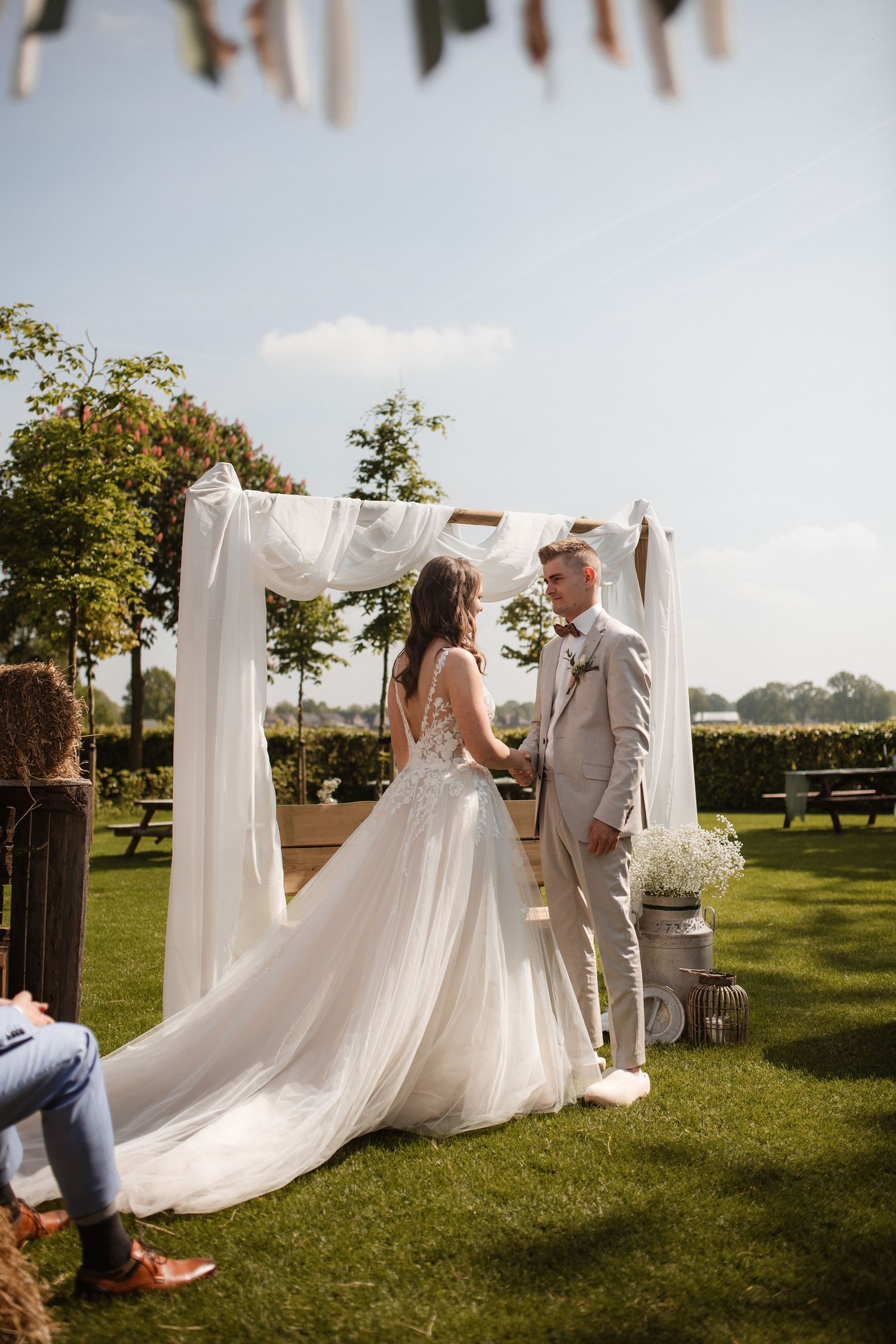 White fabric drapes create an elegant outdoor ceremony space on a sunny lawn.