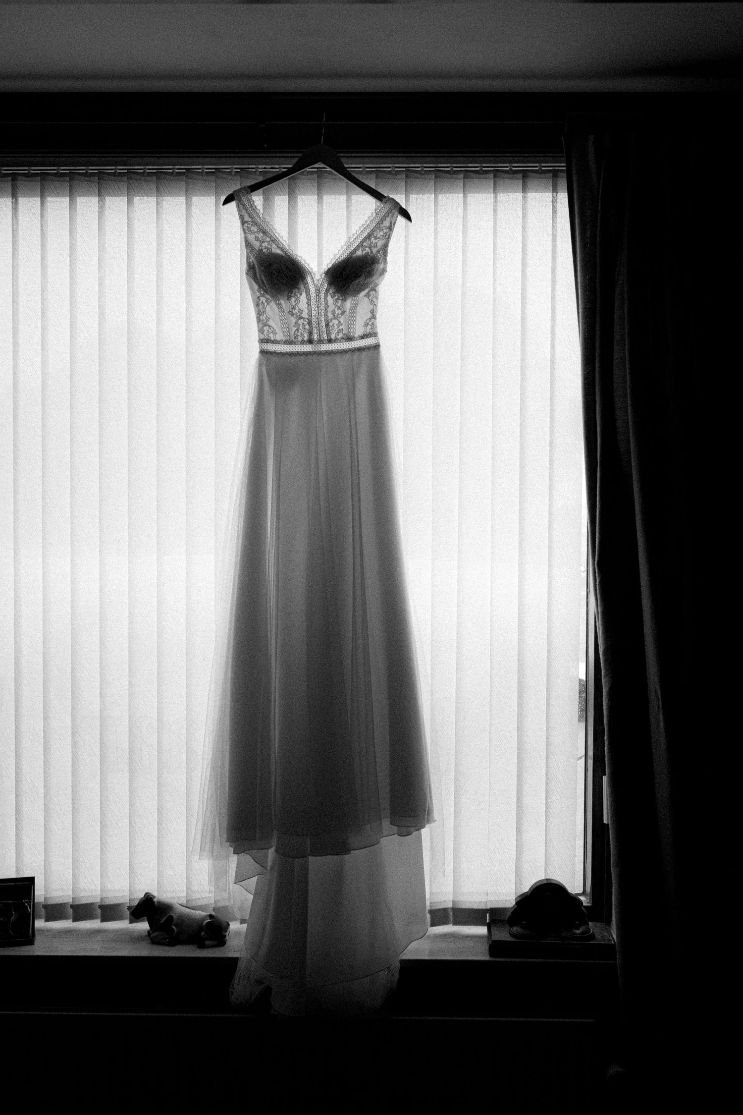 Wedding dresses hanging in silhouette against bright windows with vertical blinds.