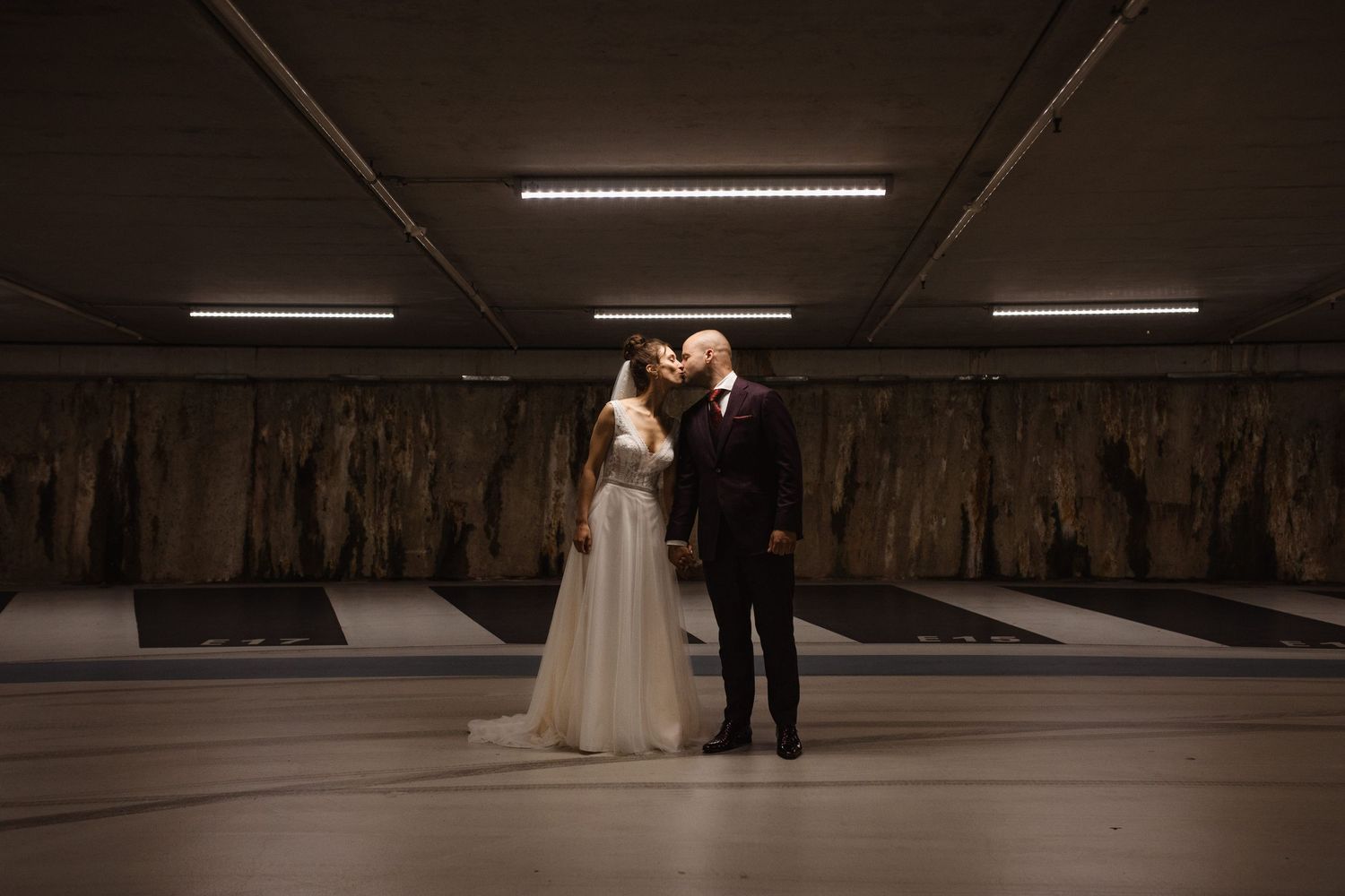 An artistic wedding photo of a couple in a dimly lit underground parking garage.