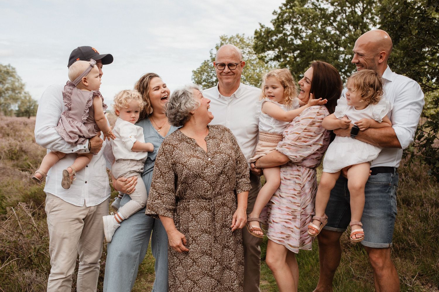 Extended family poses together outdoors in coordinated neutral outfits during a golden hour photo session.