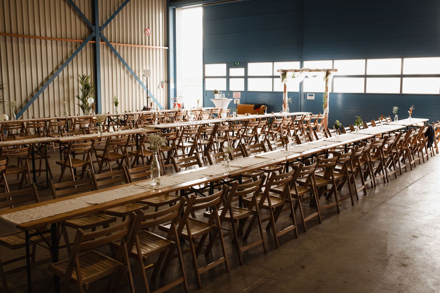 Empty wooden chairs arranged in rows inside an industrial-style wedding venue.