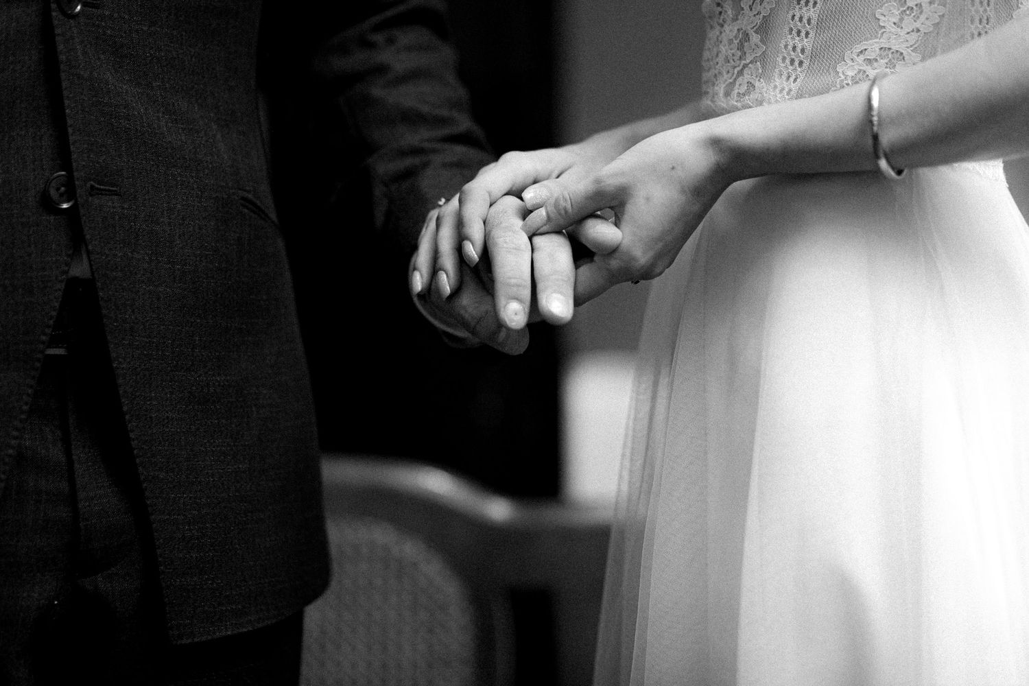 Black and white detail shot of wedding rings and hands during ceremony.