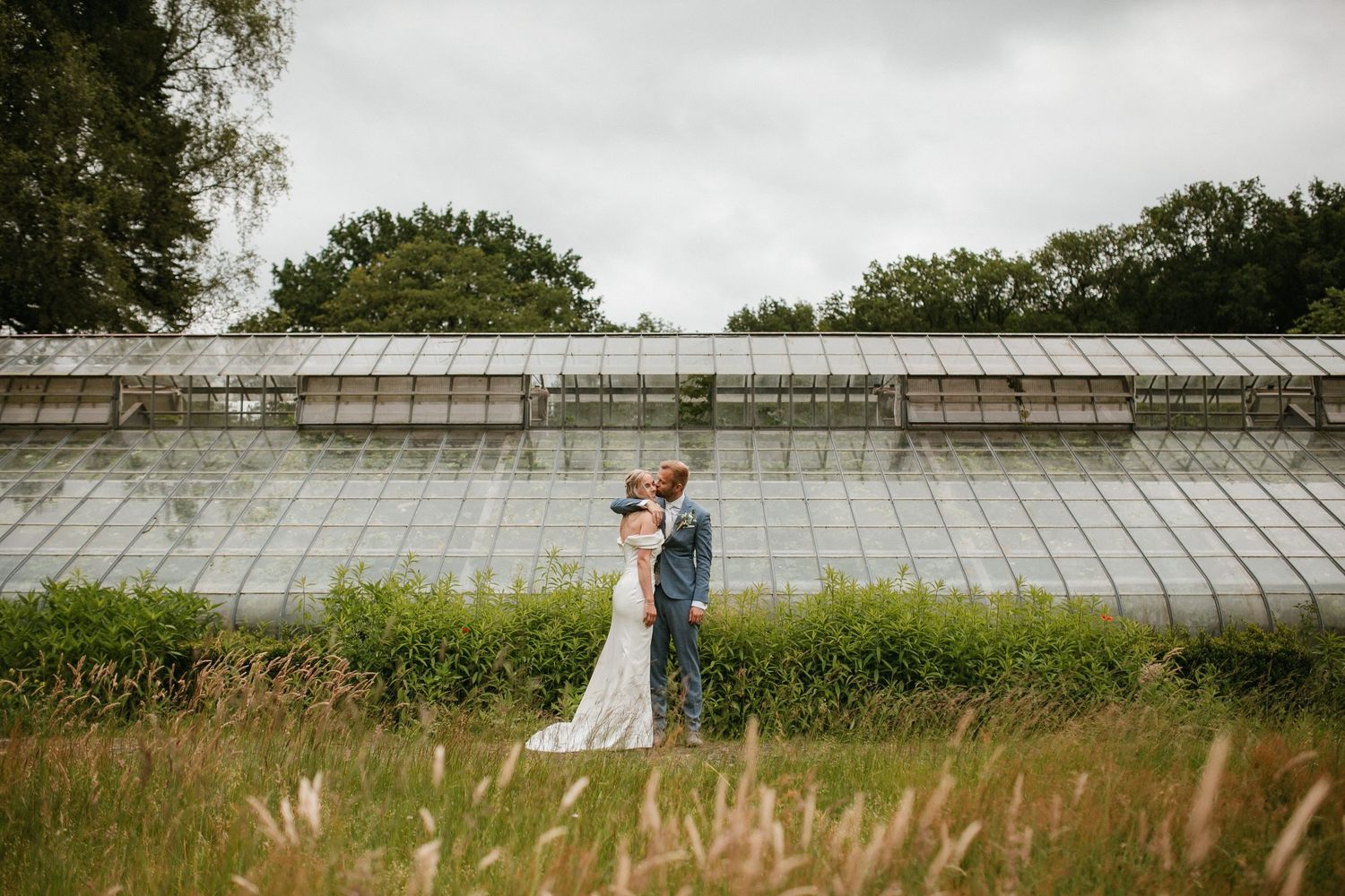 Wedding couple posing in front of a rustic stone wall with greenery.