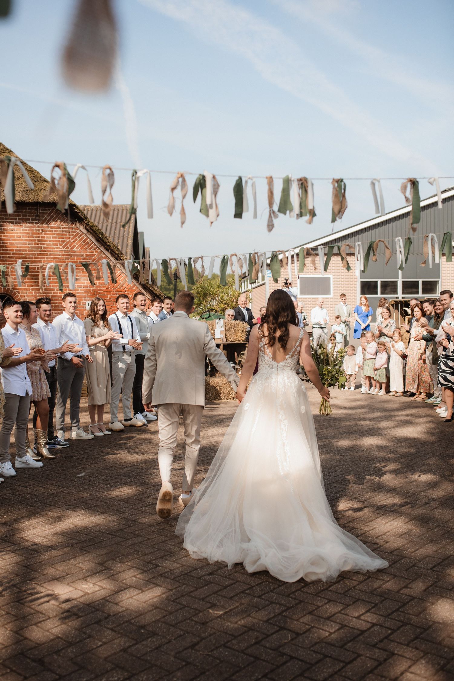 Wedding celebration with guests lining pathway under decorative banners.