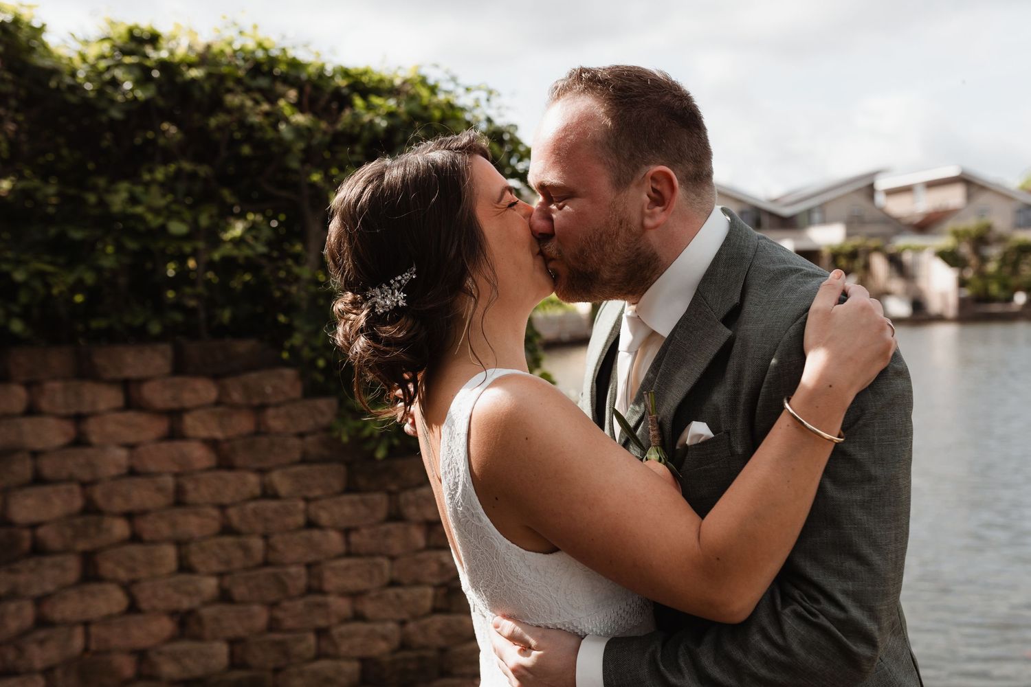 Romantic wedding portraits by a waterfront with brick wall backdrop.