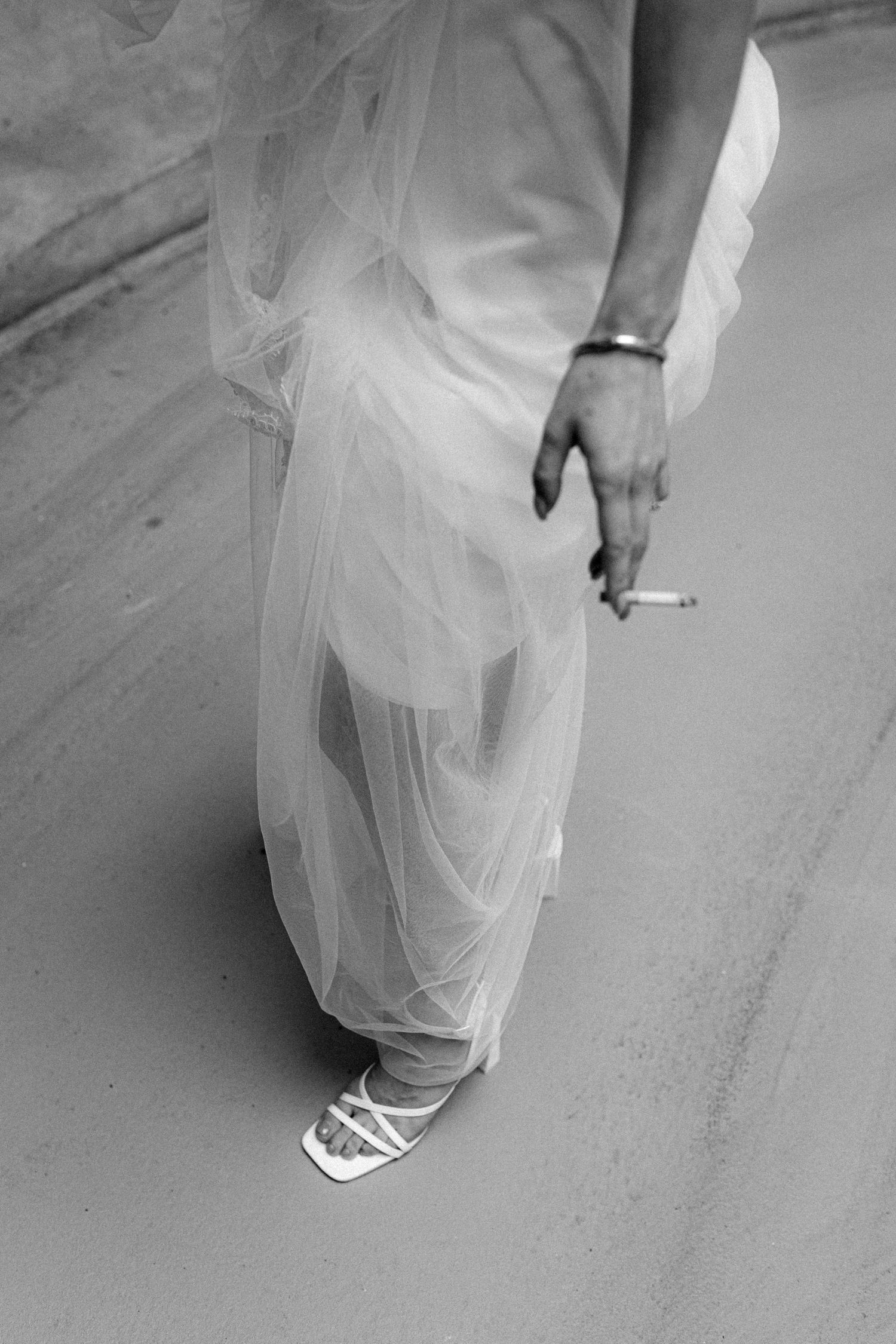 A black and white detail shot of a bride's dress hem and sneakers.