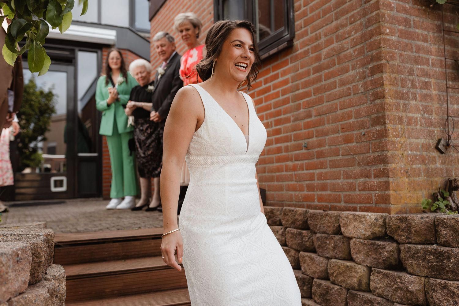 Wedding couple poses against brick wall near stone steps outdoors.
