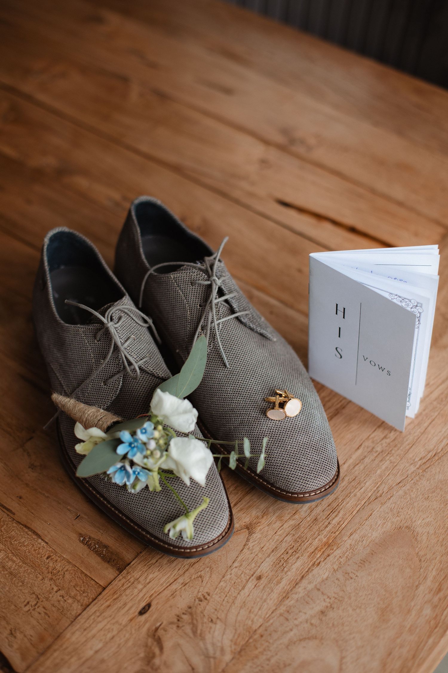 Small gray baby shoes decorated with delicate flowers displayed next to a white card on wooden surface.