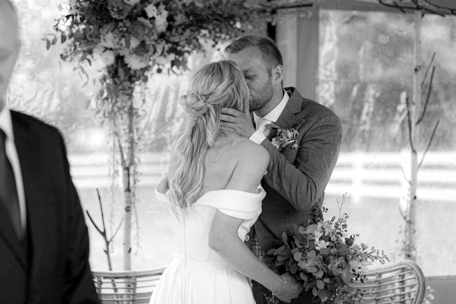 Black and white photo captures intimate wedding moments under floral archway.