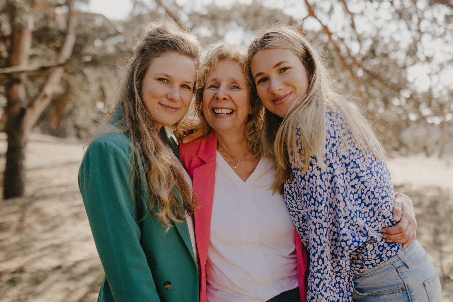 Three friends in colorful outfits smiling together outdoors in natural lighting.