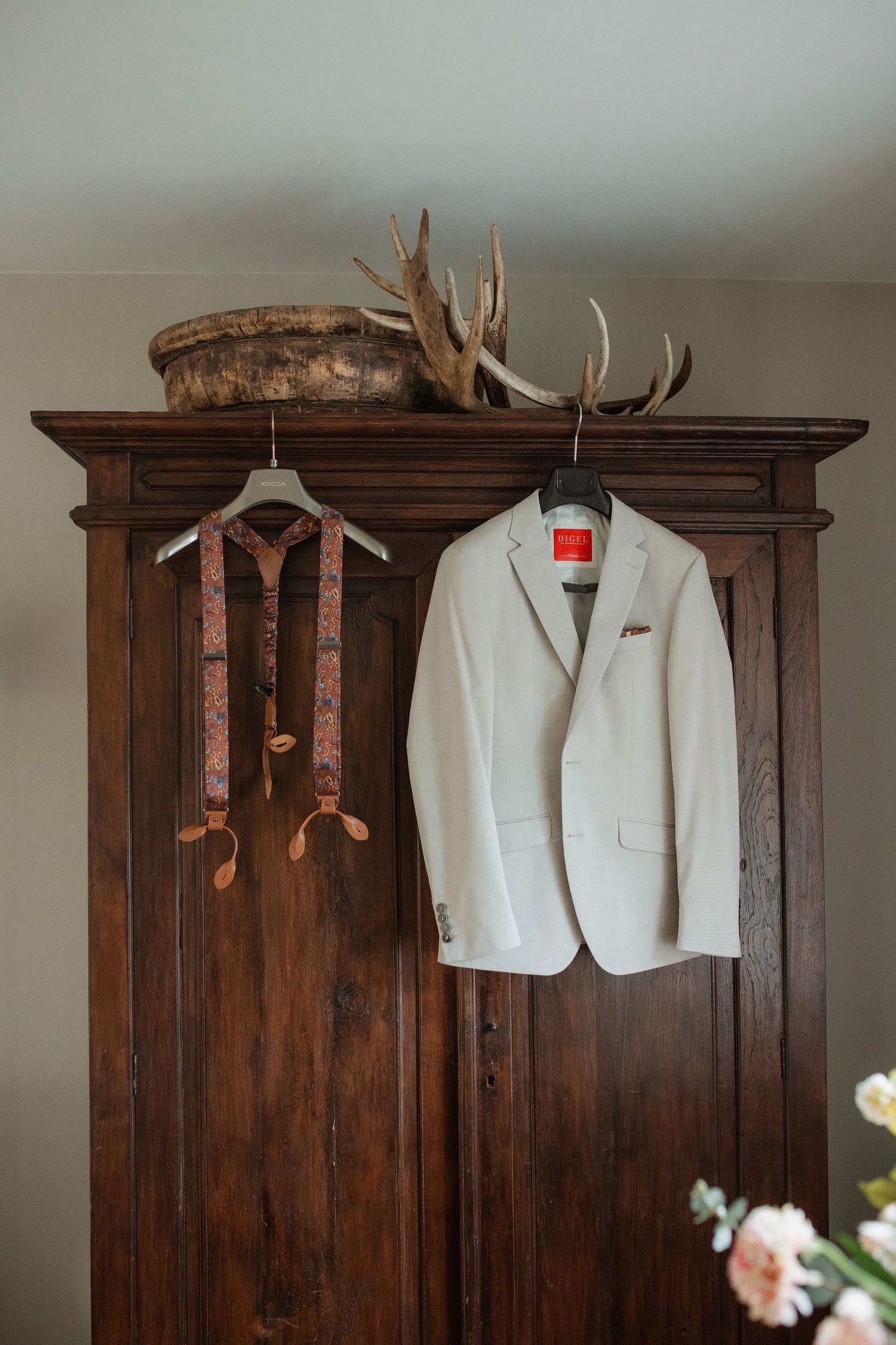 A white wedding jacket hangs on a rustic wooden wardrobe with antler decorations.
