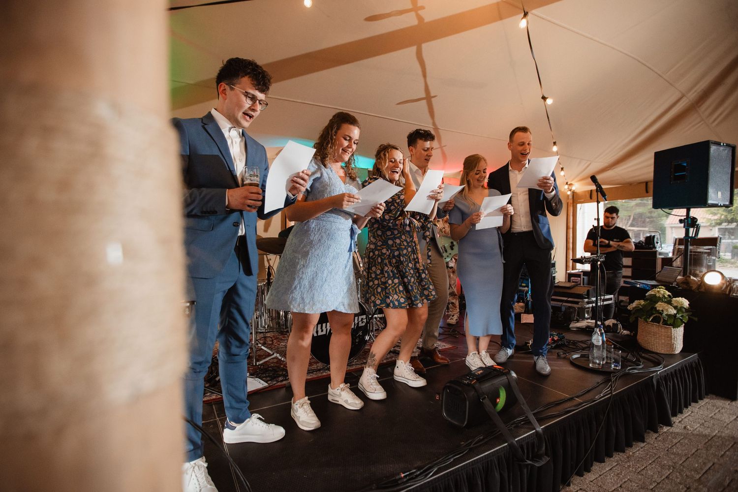 Wedding guests dancing and celebrating under large white tent with string lighting.