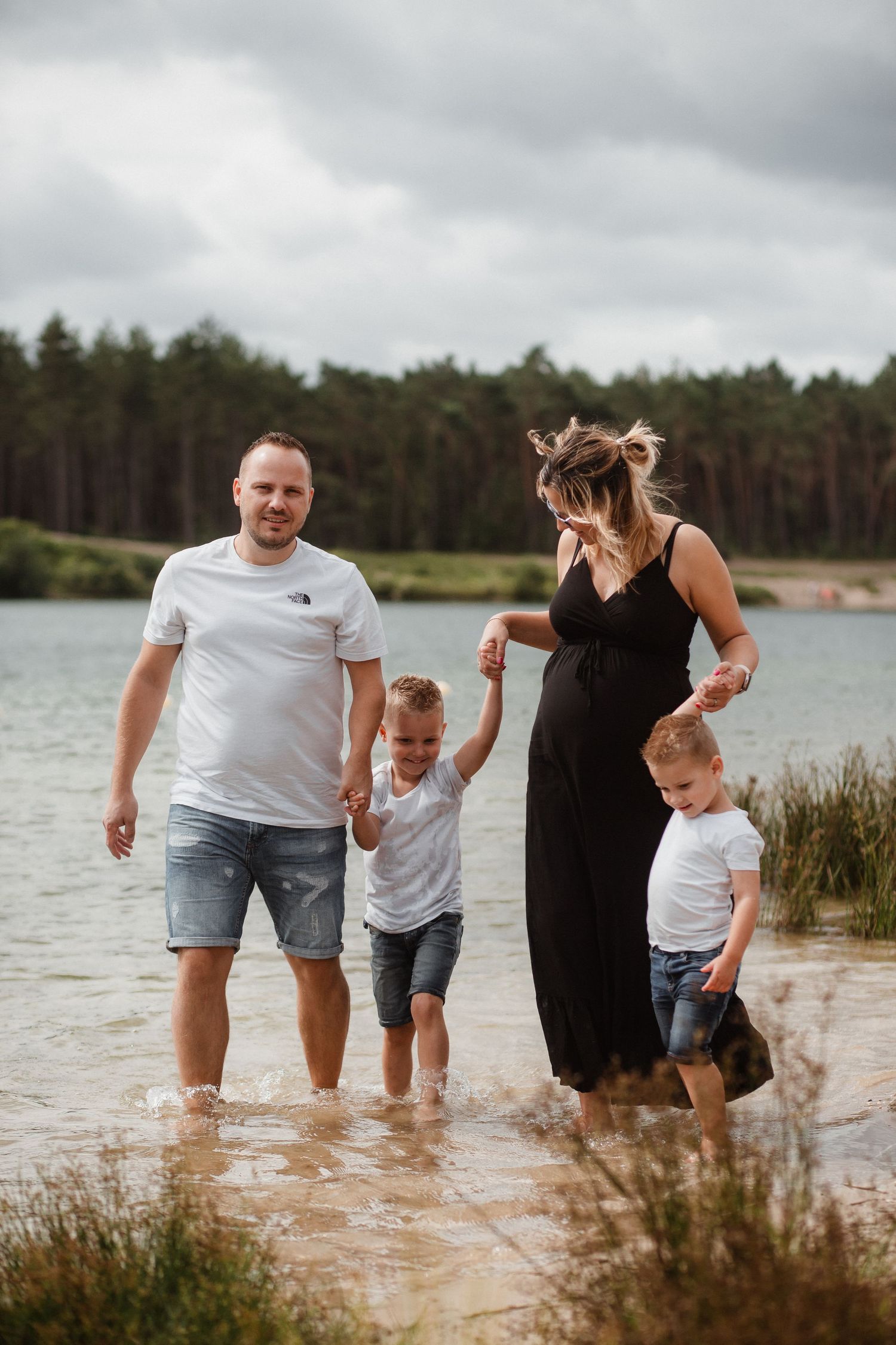 Family splashing and playing in shallow lake water on a cloudy day.