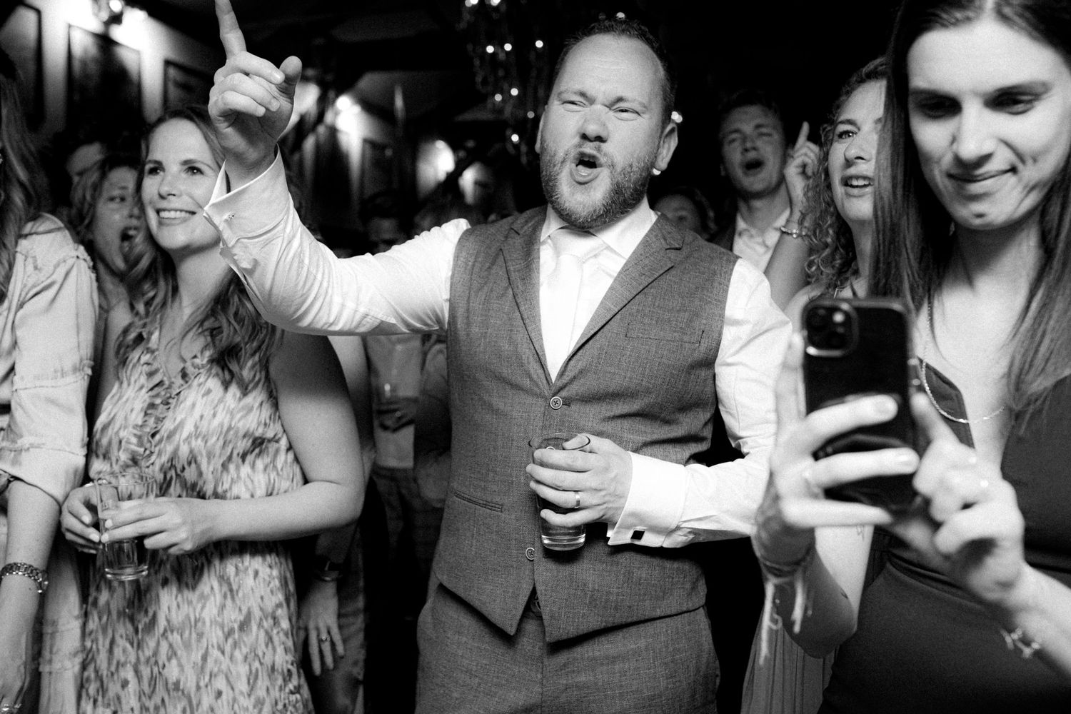 Black and white photo of people dancing and celebrating at a festive gathering.