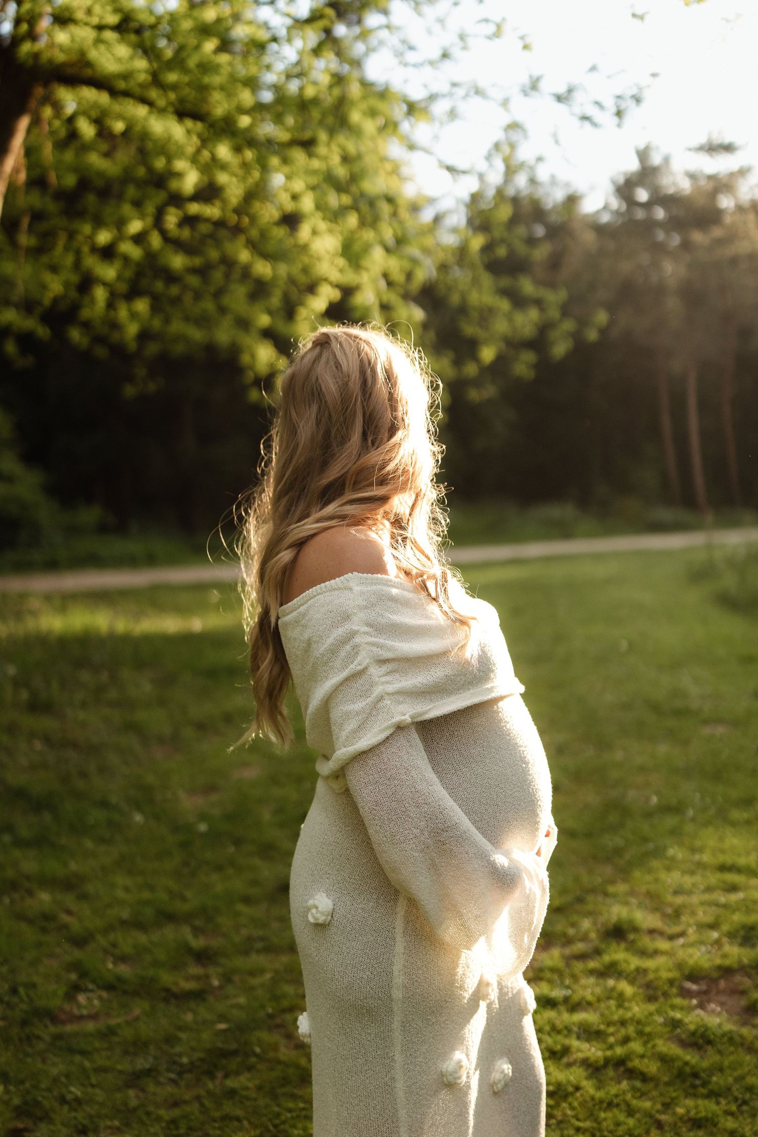 Een zwangere vrouw poseert in de natuur tijdens golden hour.