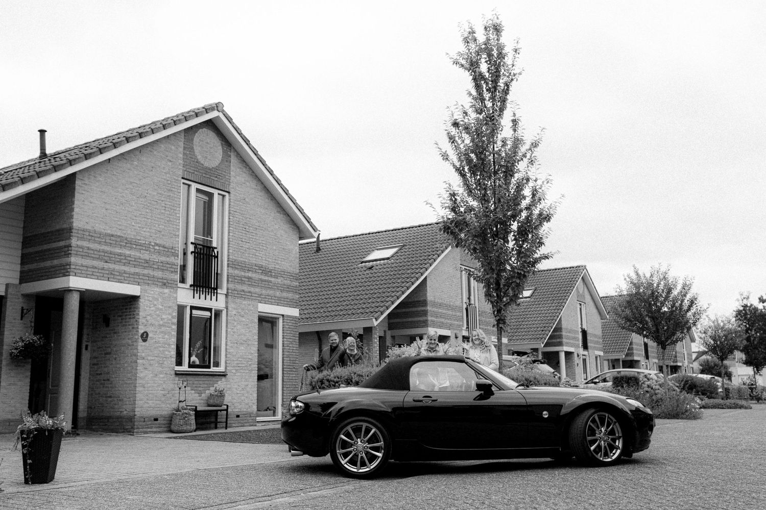 A black sports car parked in front of modern suburban houses on a residential street.