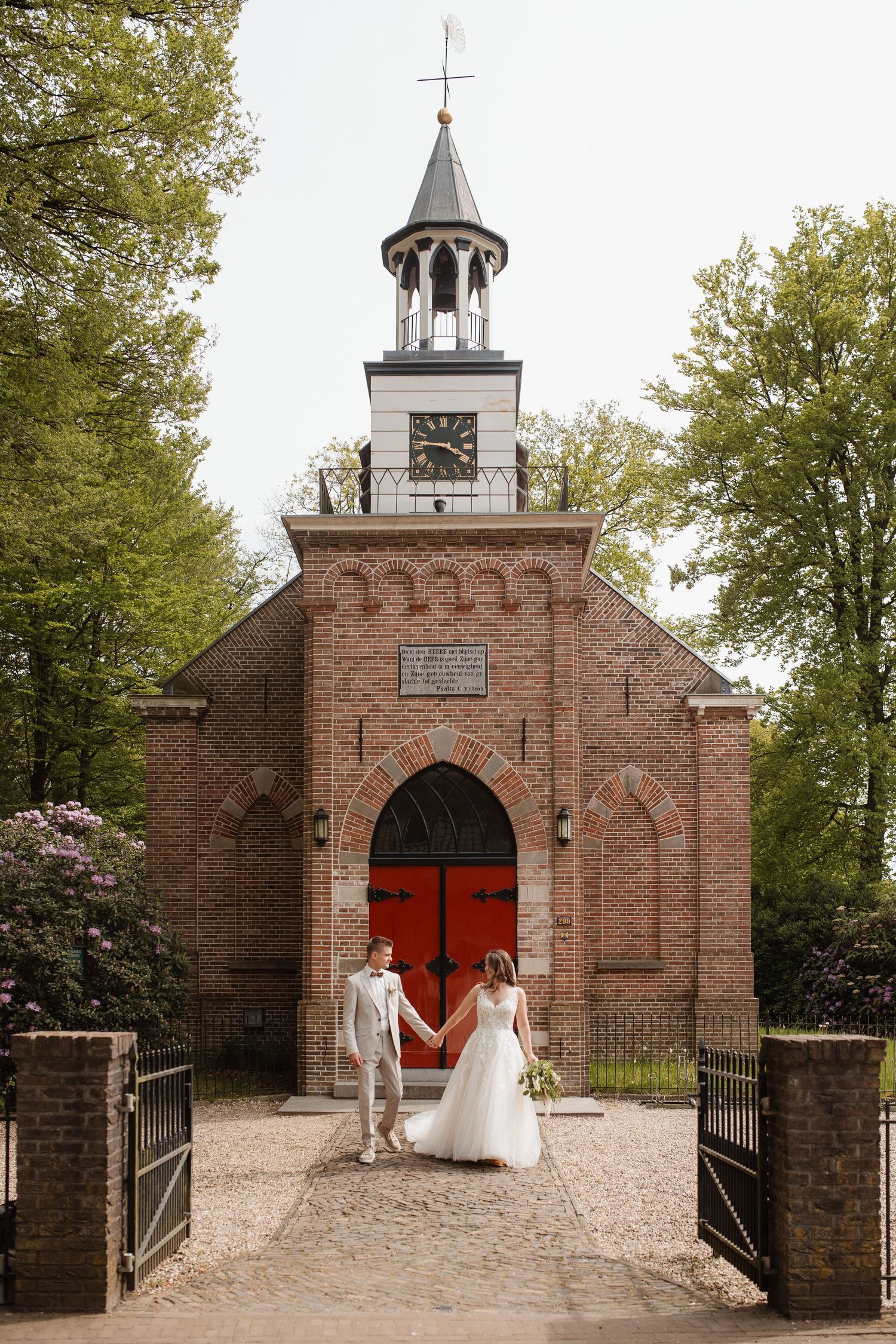 Beautiful brick chapel with red doors and bell tower serves as backdrop for wedding portraits.