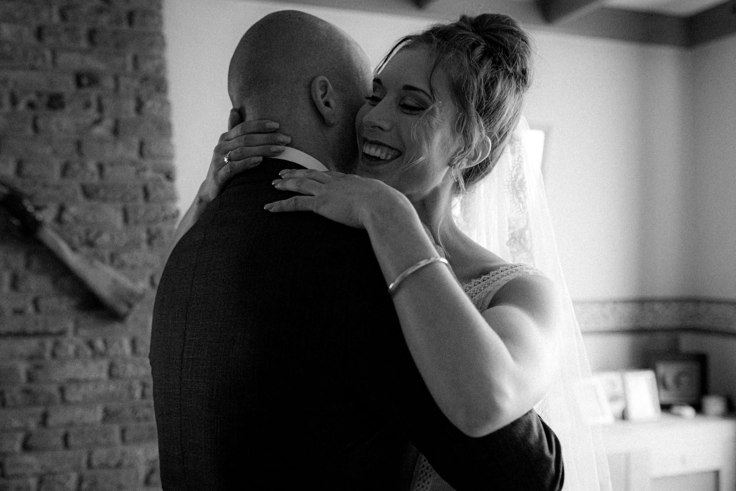 Black and white photograph of an intimate wedding moment against a brick wall.