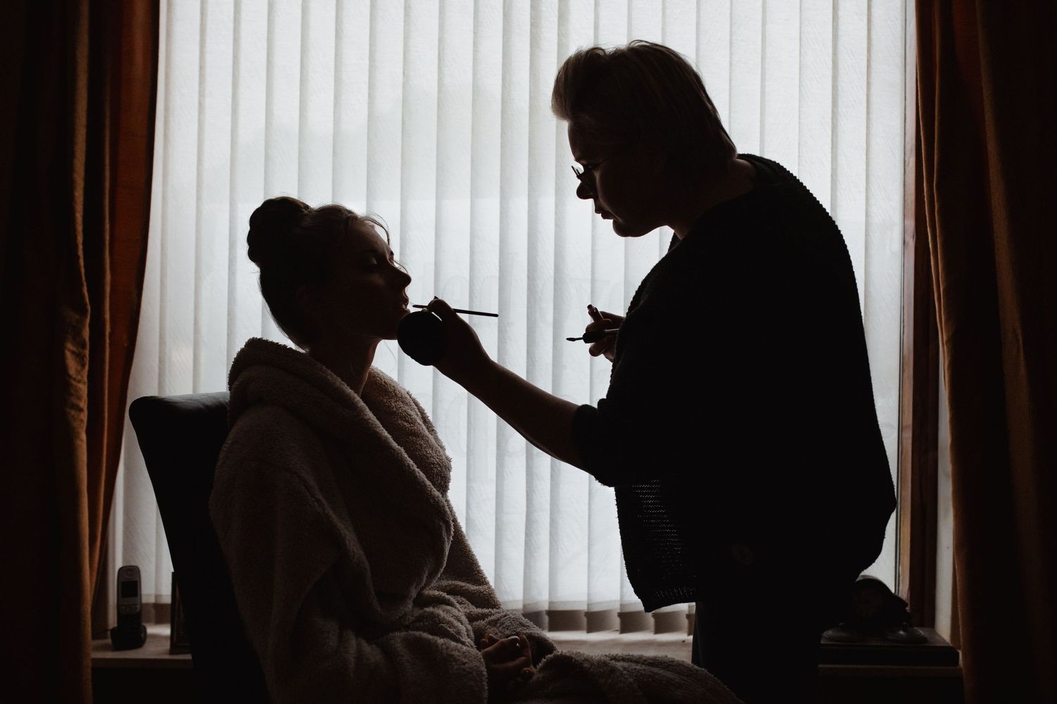 Silhouettes of people getting ready against a window with vertical blinds.