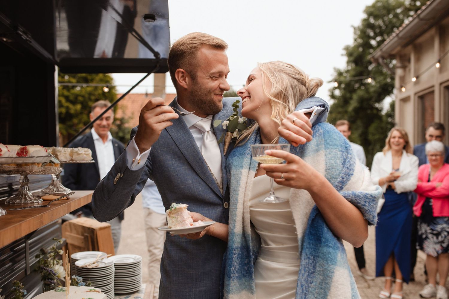 Wedding celebration scene with guests dancing and embracing at an outdoor venue.