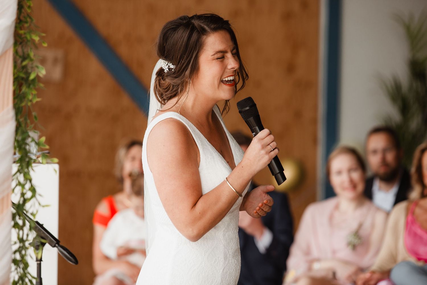 A wedding celebration with guests laughing and enjoying speeches in an indoor venue.