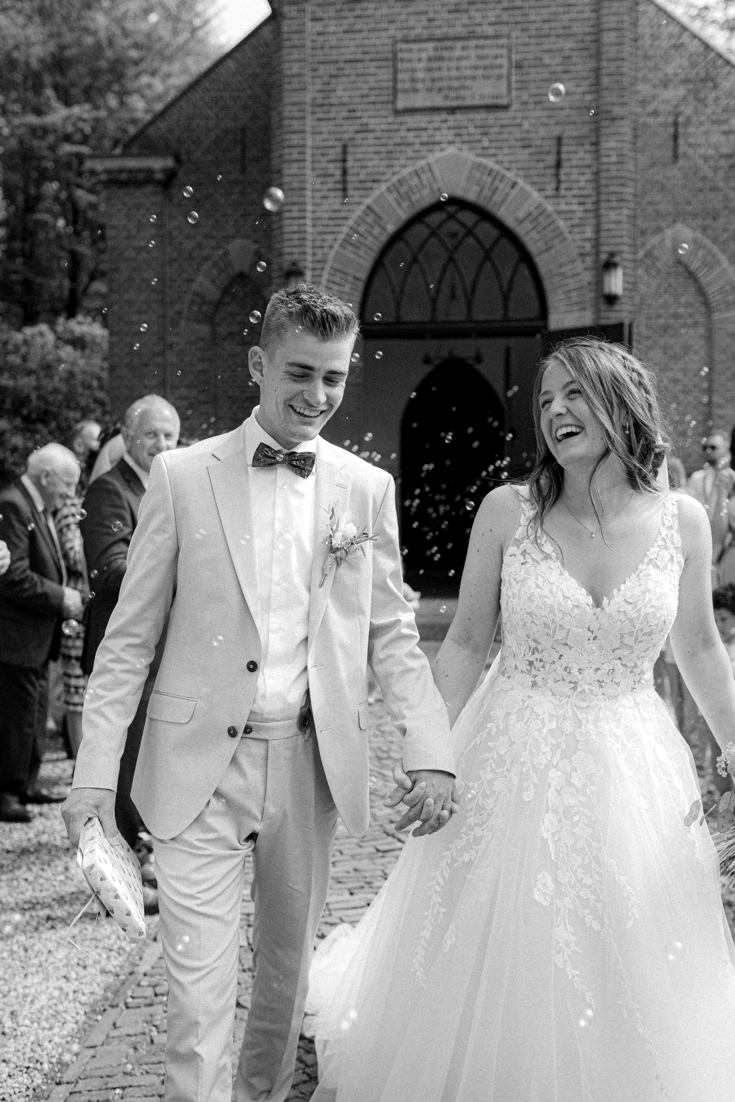 Joyful wedding celebration outside historic brick church with confetti in black and white.