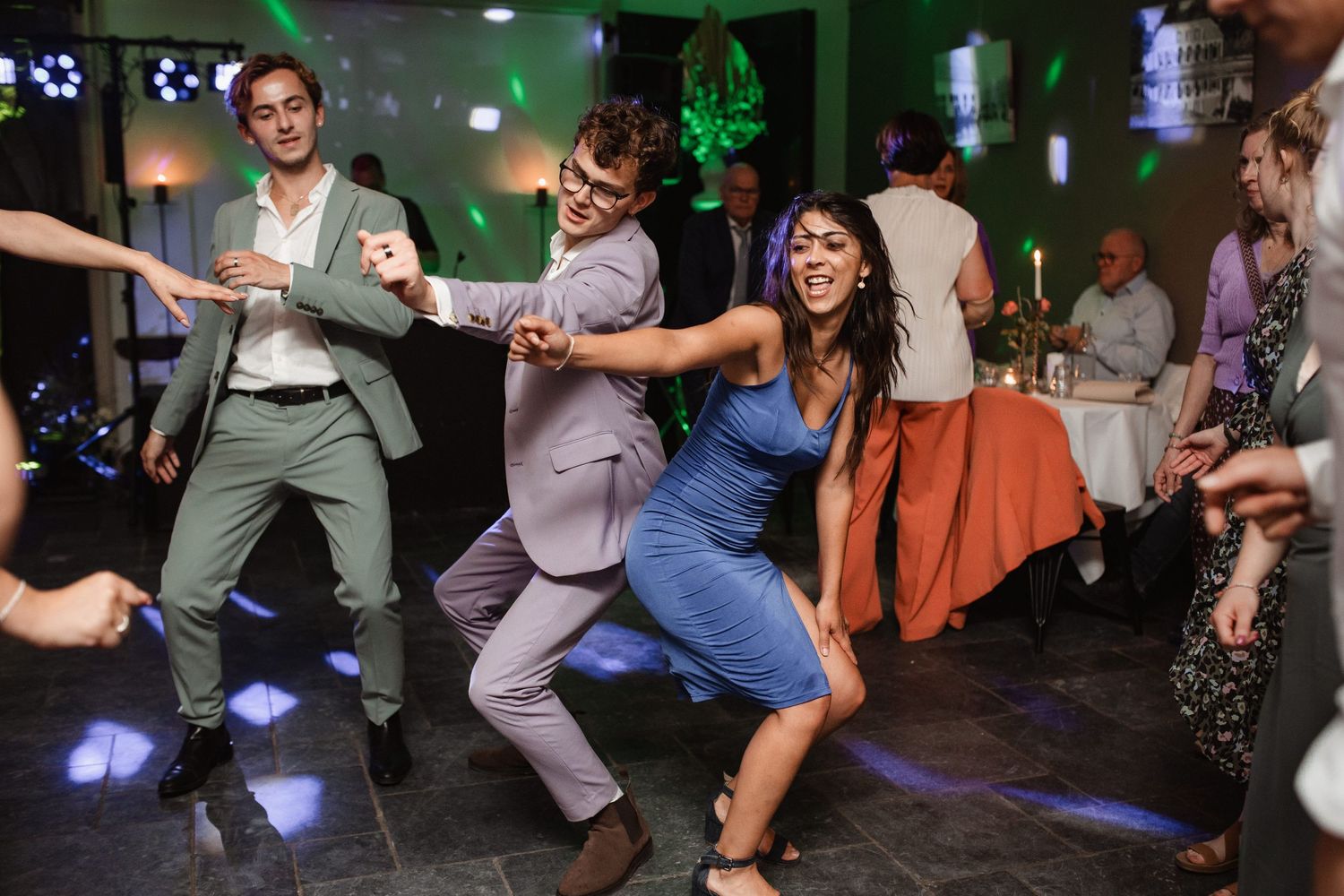 Wedding guests dancing and having fun under colorful party lights.
