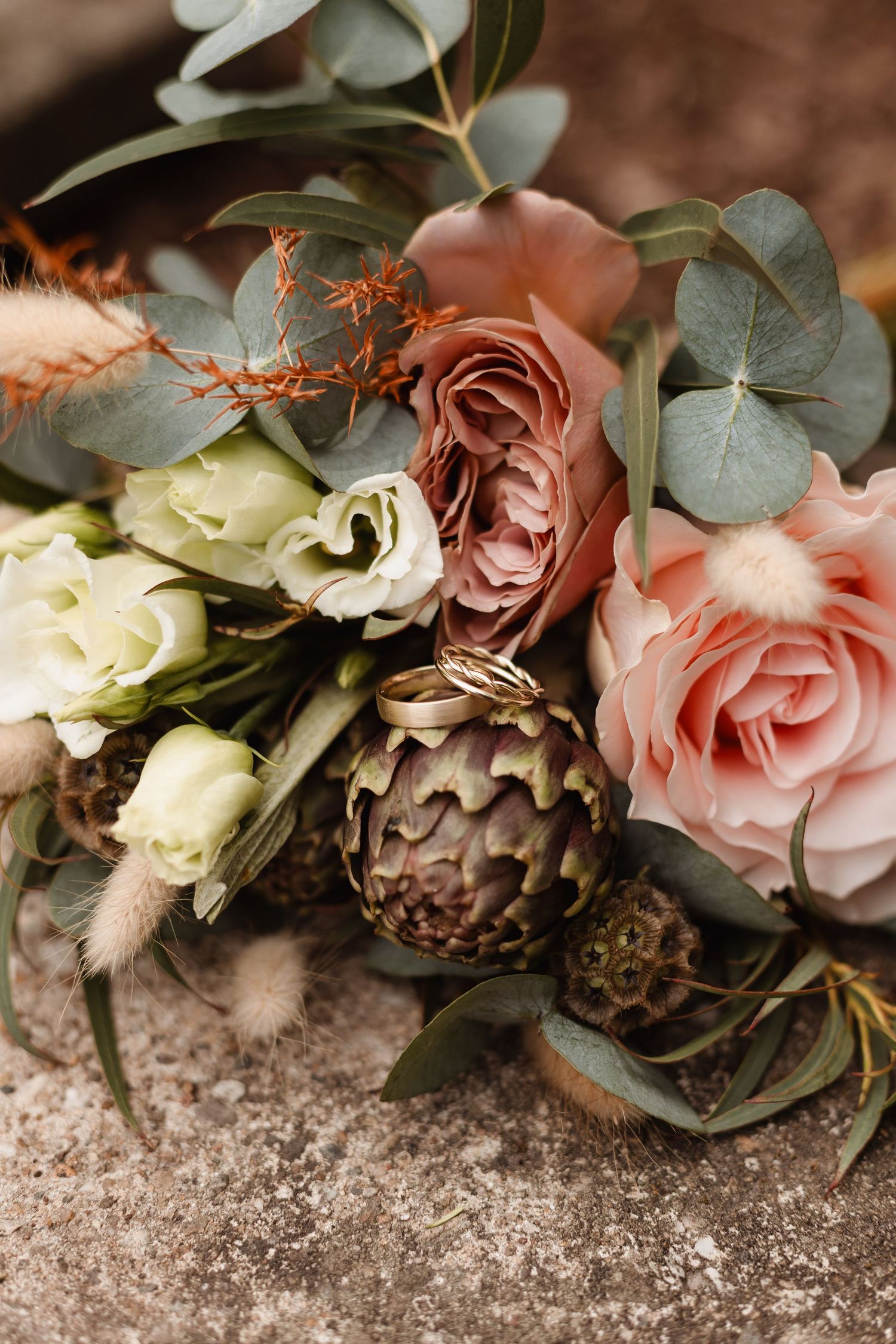 Romantic floral arrangement with pink roses and eucalyptus on stone surface.