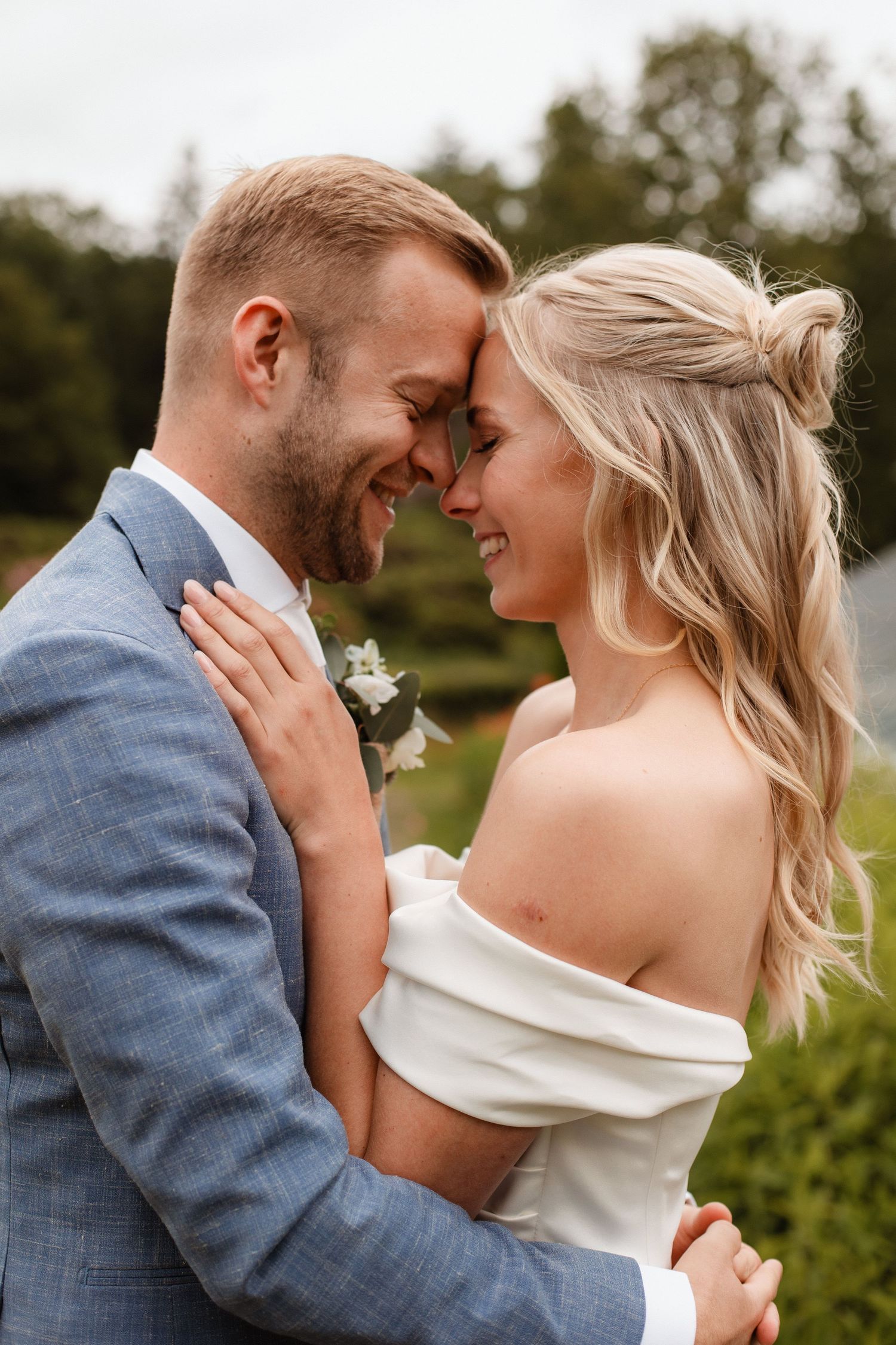 Tender moment between newlyweds in an outdoor garden setting.