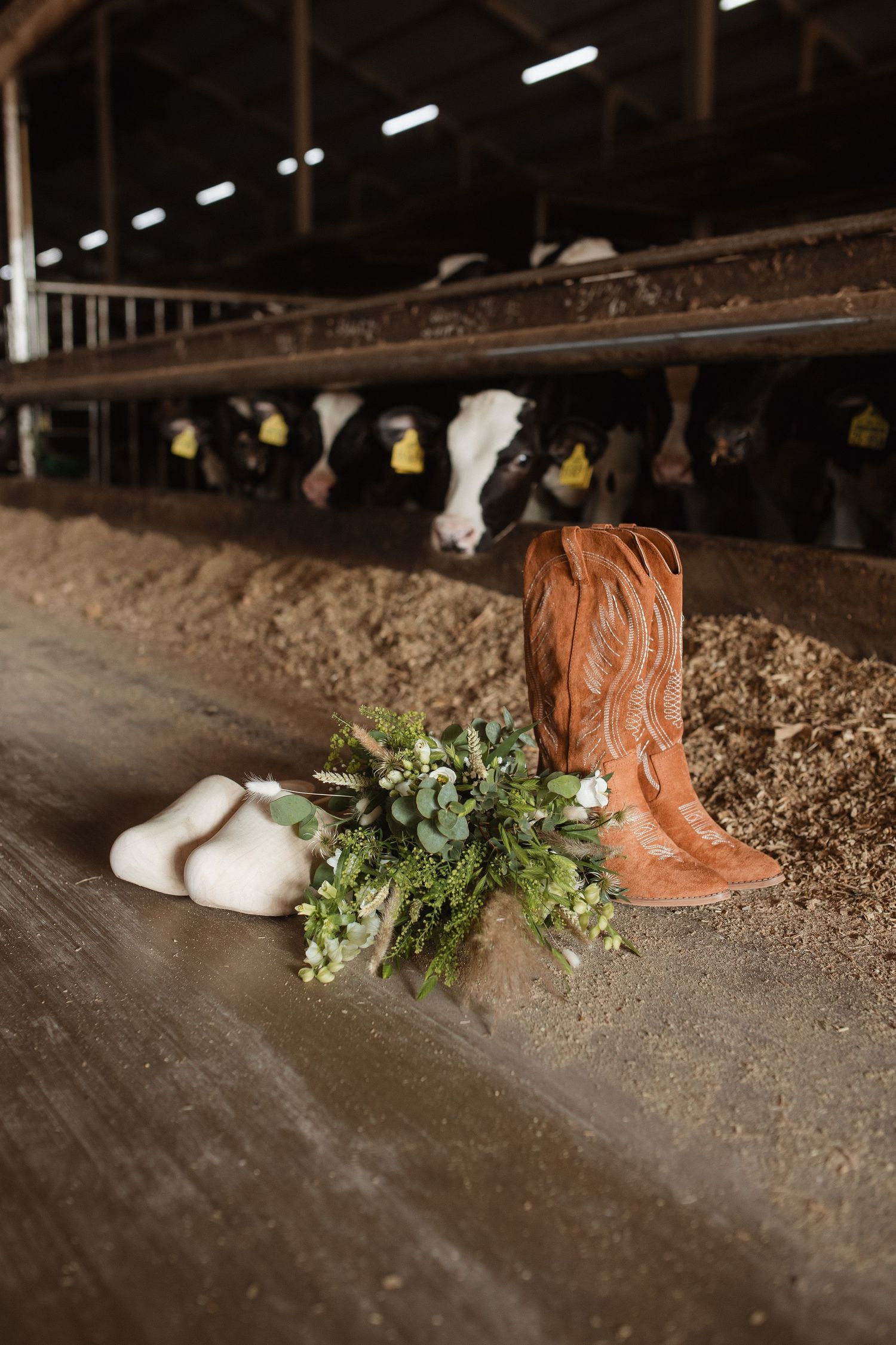 Wedding details with cowboy boots, greenery and decor on rustic wooden surface.