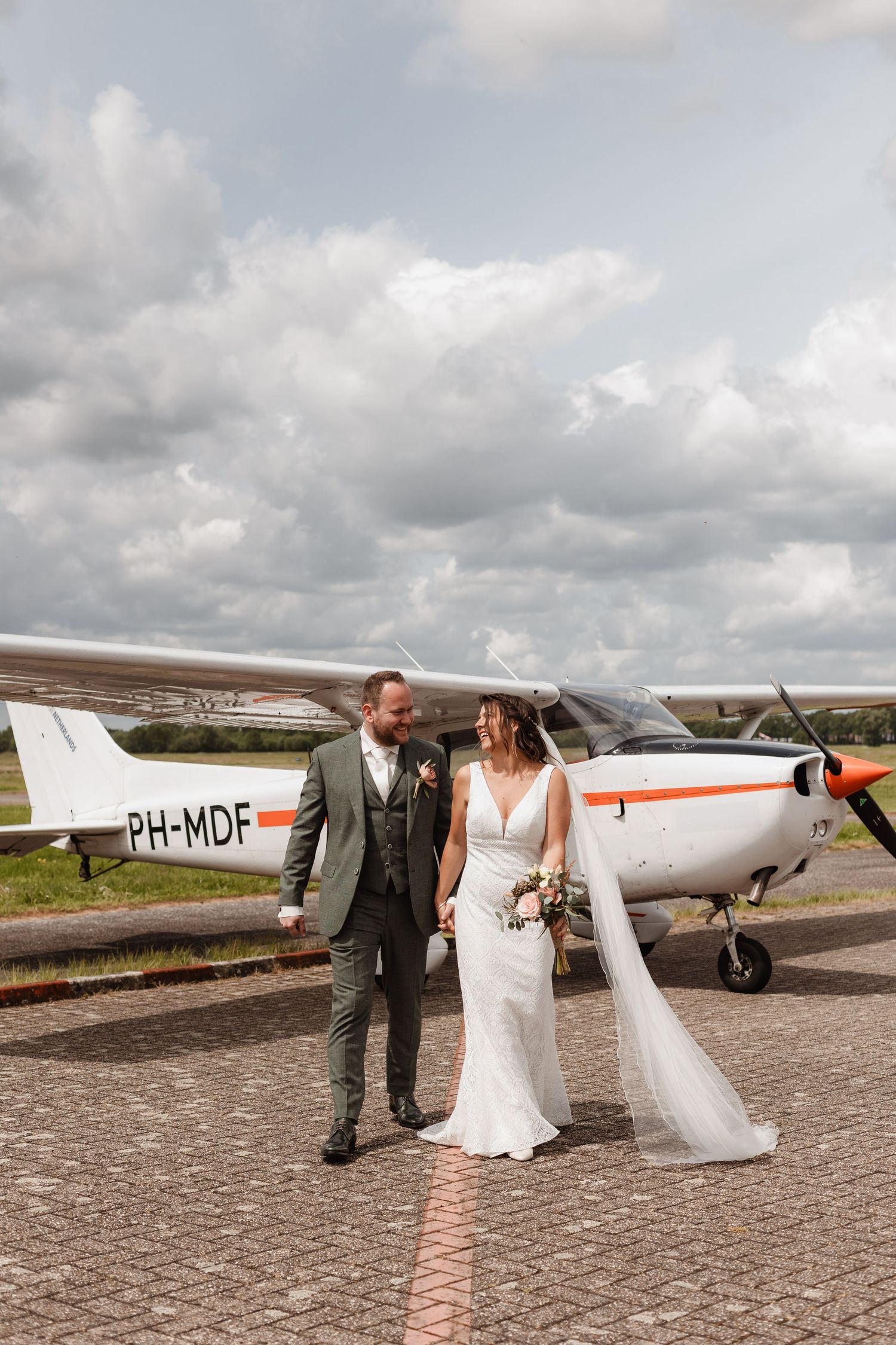 Wedding couple poses next to small aircraft on airfield tarmac.