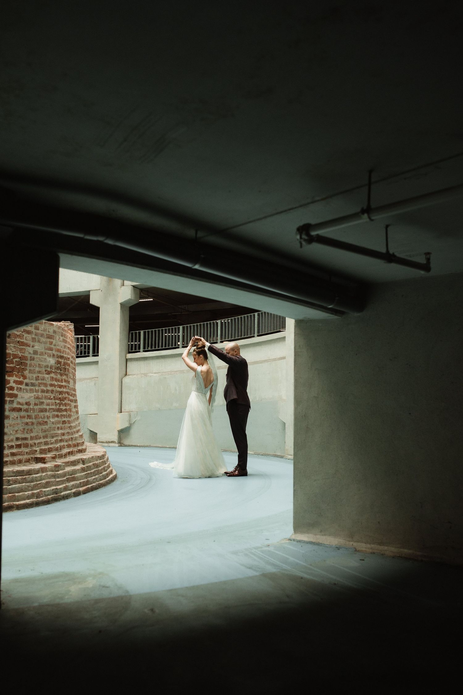 A couple dances in an atmospheric underground parking structure with dramatic lighting.