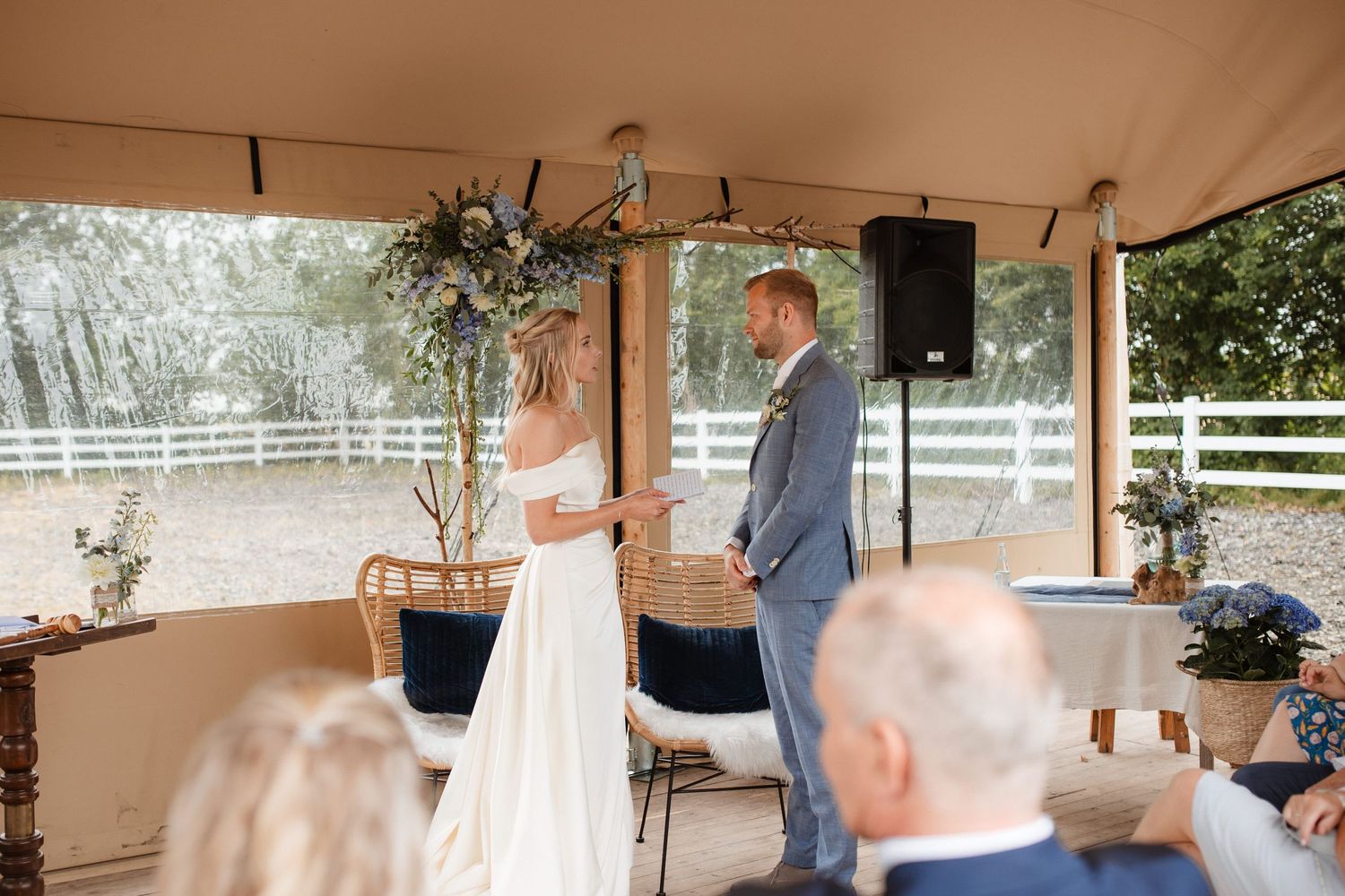 A couple shares a playful moment during their first dance at an outdoor covered venue with white decor.