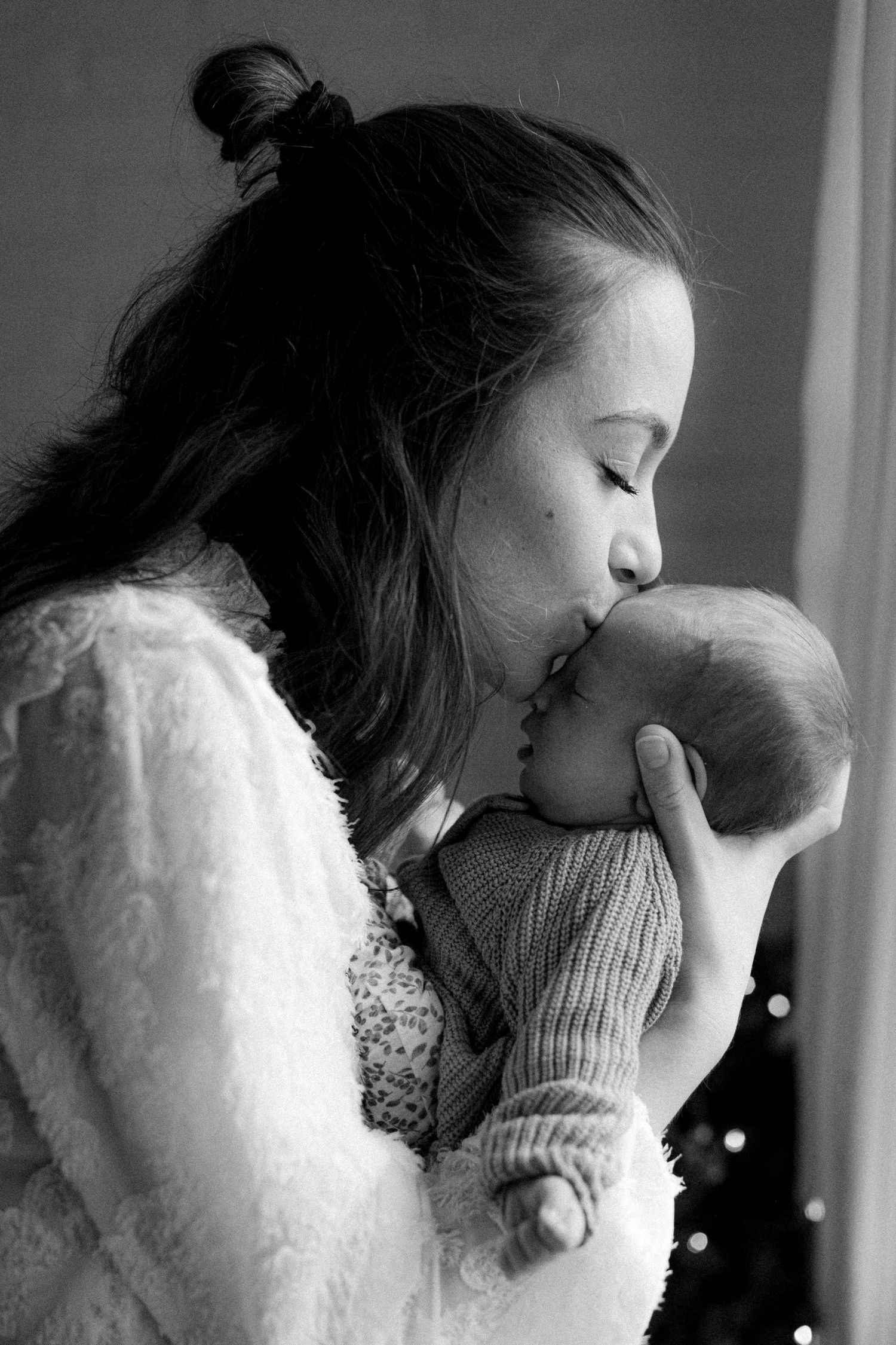 Moeder geeft haar baby een kus tijdens een newbornshoot thuis