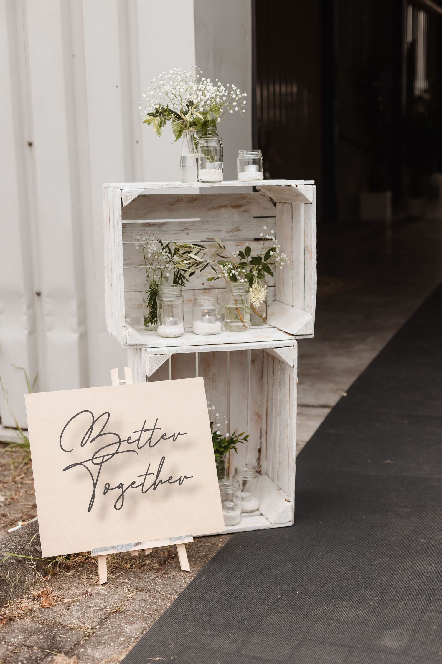 Rustic white wooden crates with delicate floral arrangements and calligraphy signs create an elegant display.
