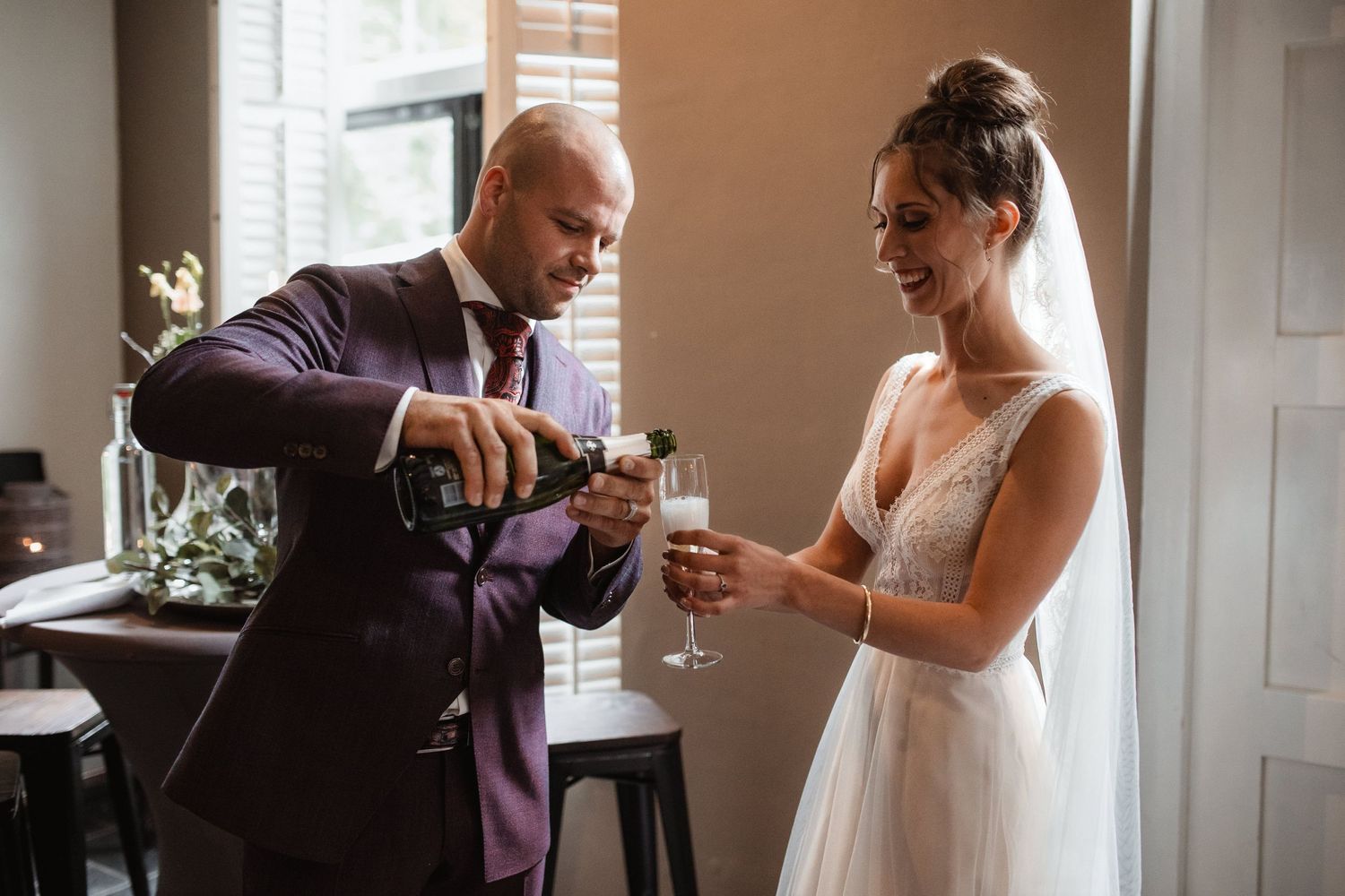 Bride and groom share intimate moment during wedding reception by window light.