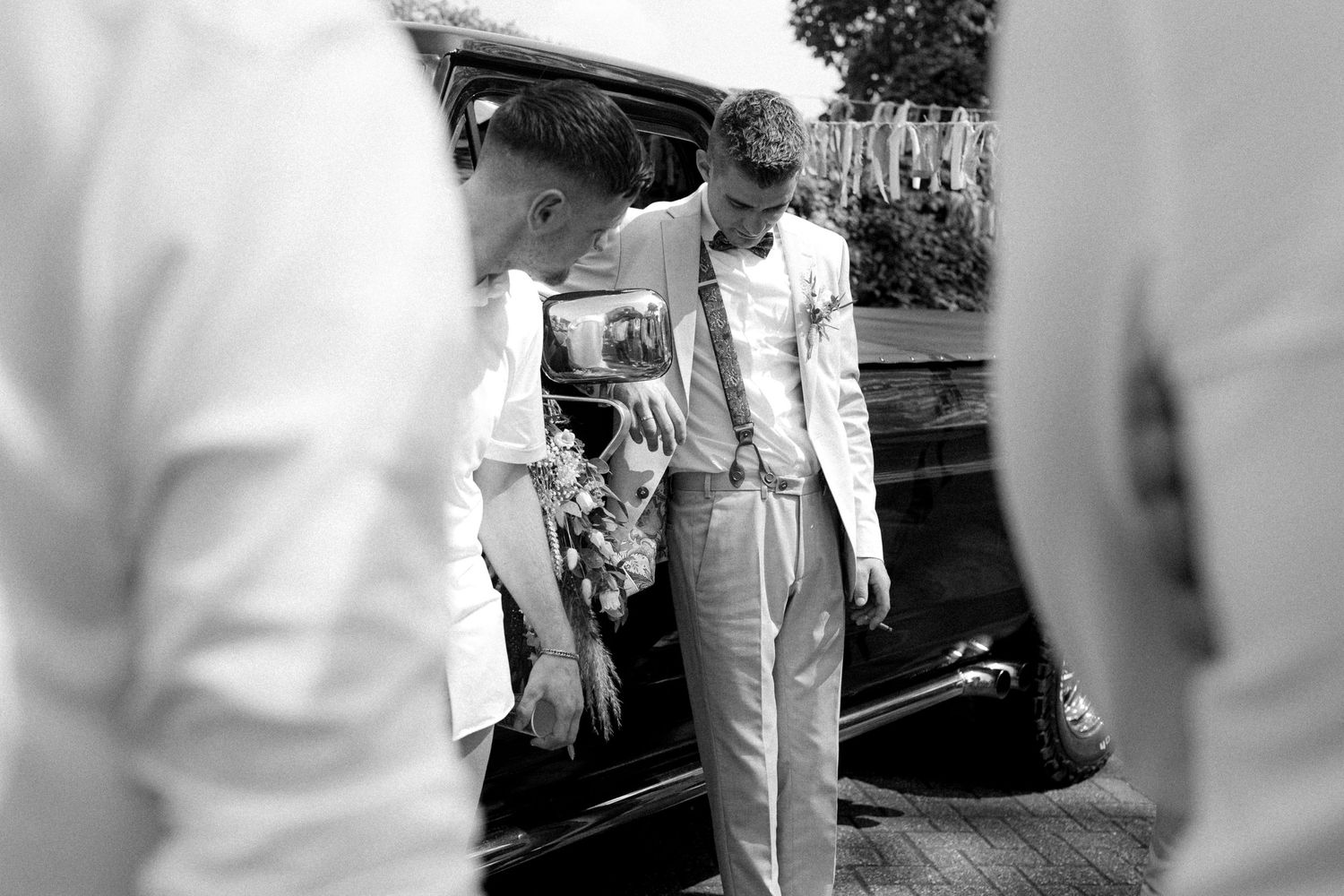 Wedding guests in white attire gathered outside near parked cars.