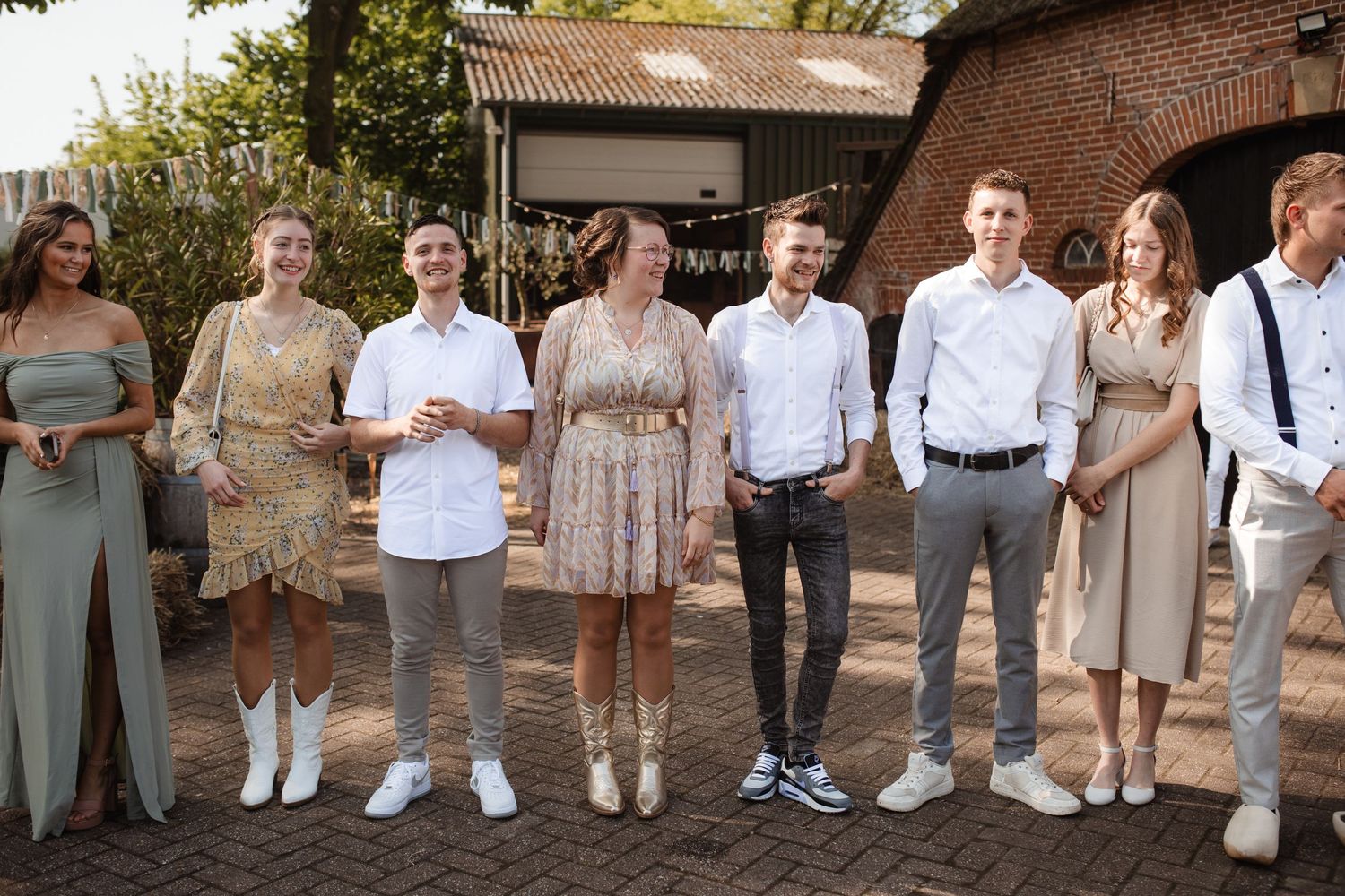 Wedding party lineup in casual attire against brick building exterior.