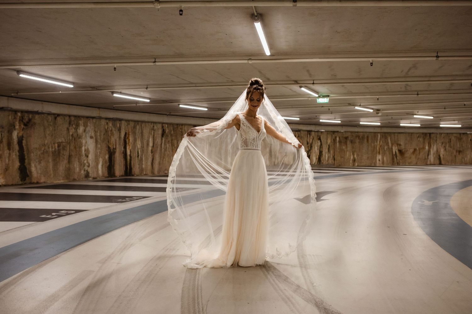 A flowing white wedding dress train spreads across a concrete floor in dramatic lighting.
