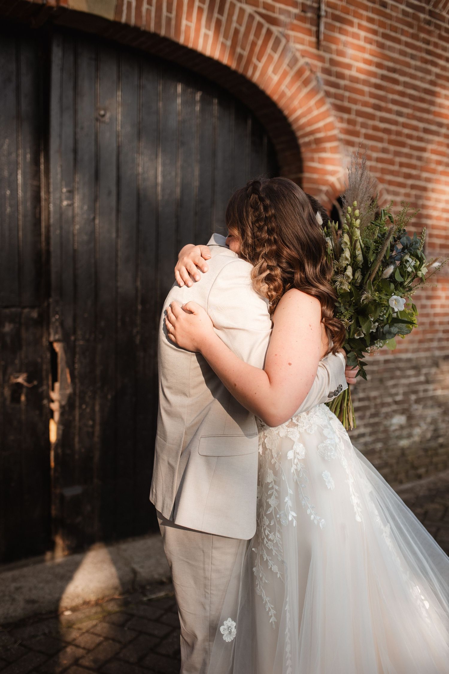 A romantic wedding moment against a rustic brick wall with dark wooden panels.