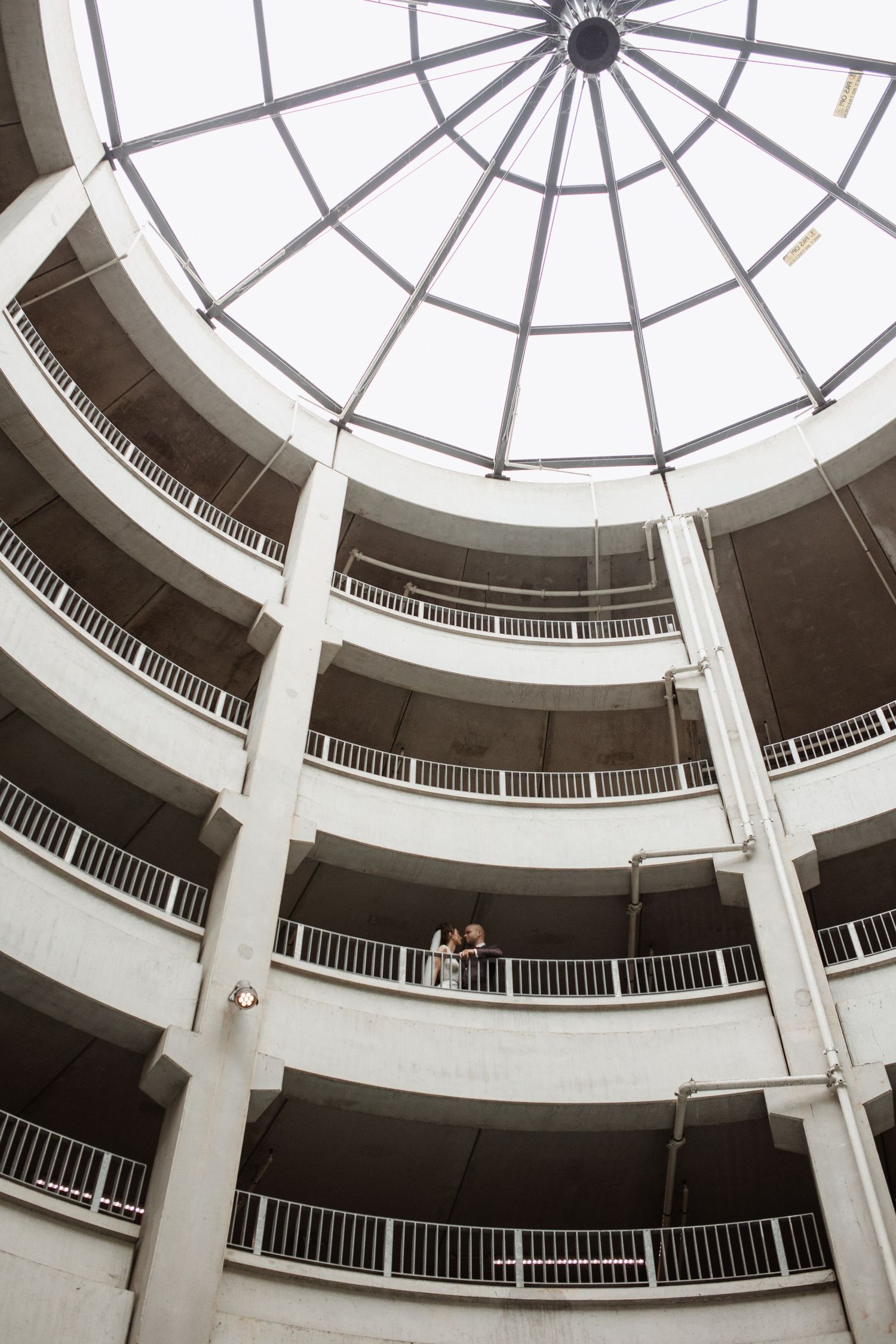Wedding couple photographed in a striking circular architectural space with dramatic skylight.