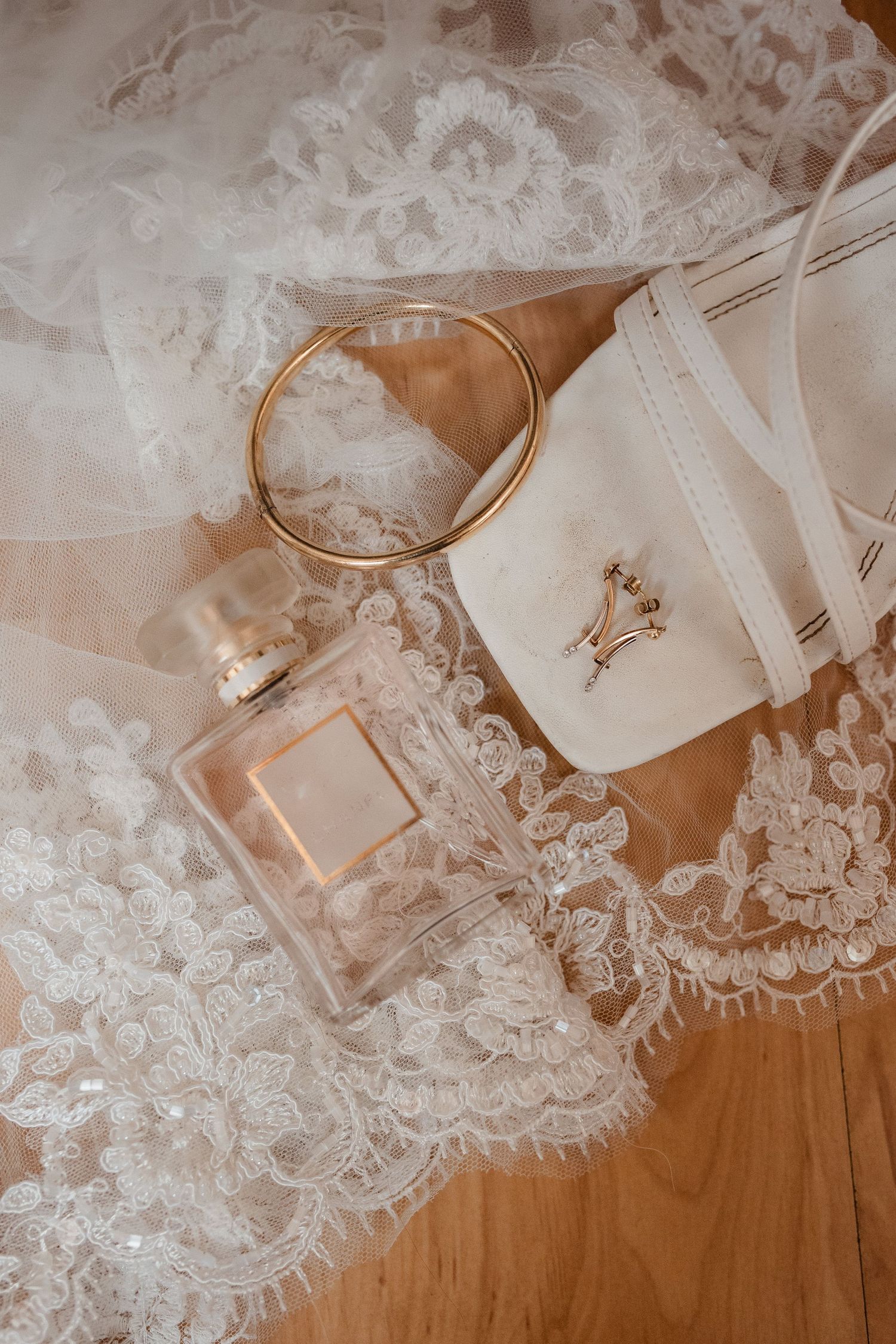 Delicate lace wedding accessories and details laid out on a wooden surface.