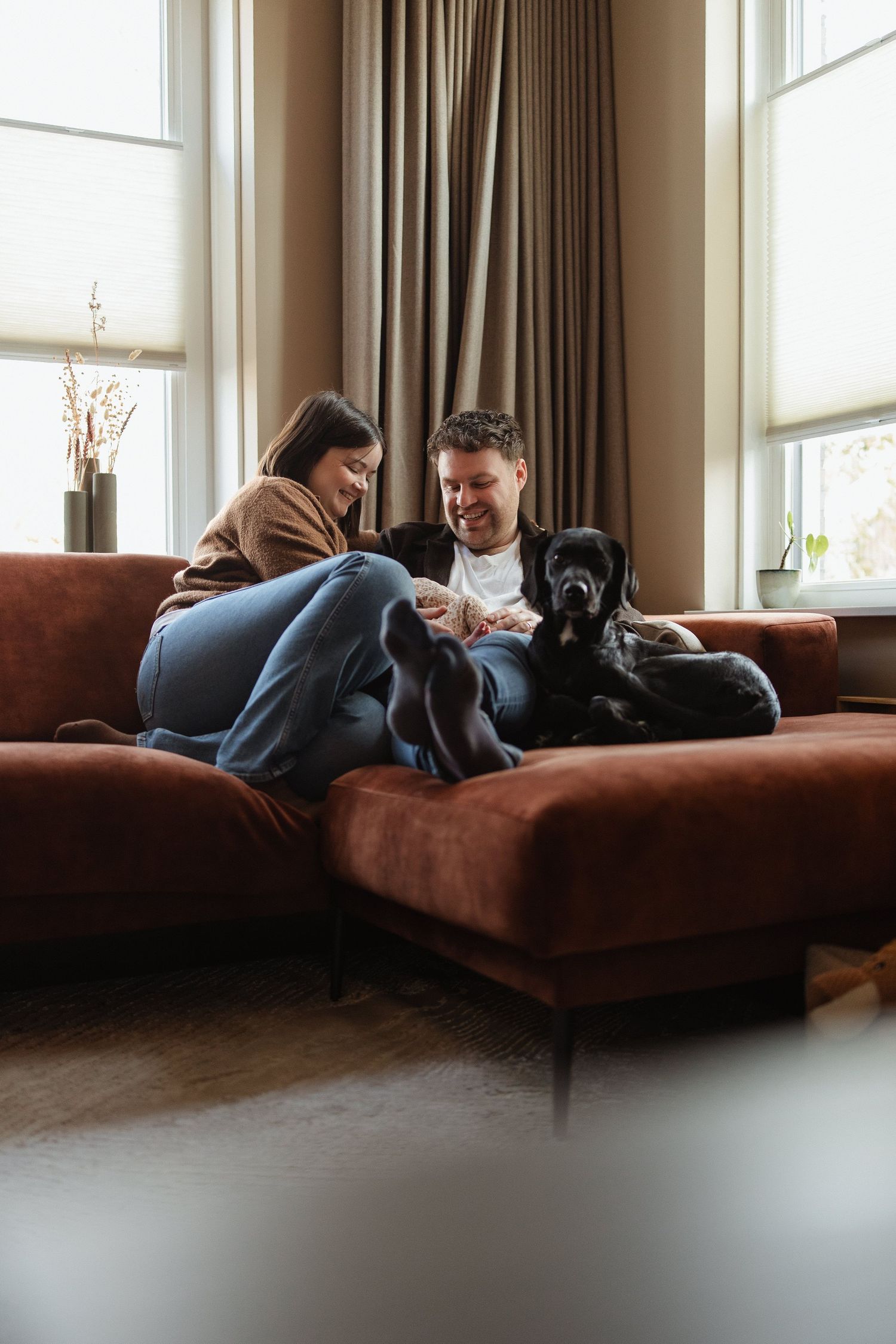 Gezinsfoto met newborn en een hond die op de bank ligt.