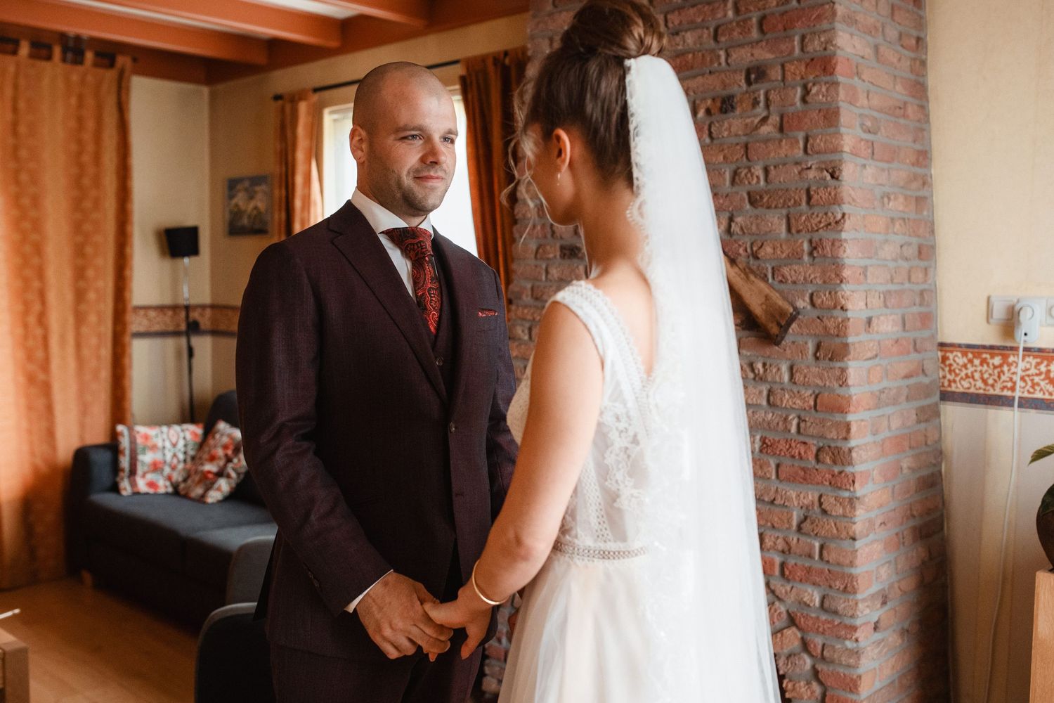 A couple shares an intimate moment in formal wedding attire against a rustic brick wall backdrop.
