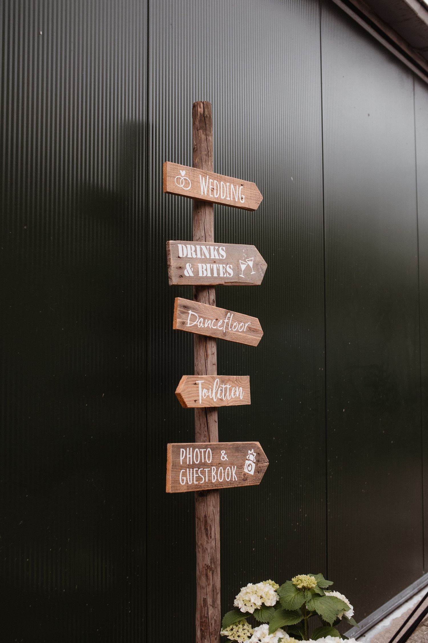 Rustic wooden directional sign post with wedding-related signs pointing different directions.