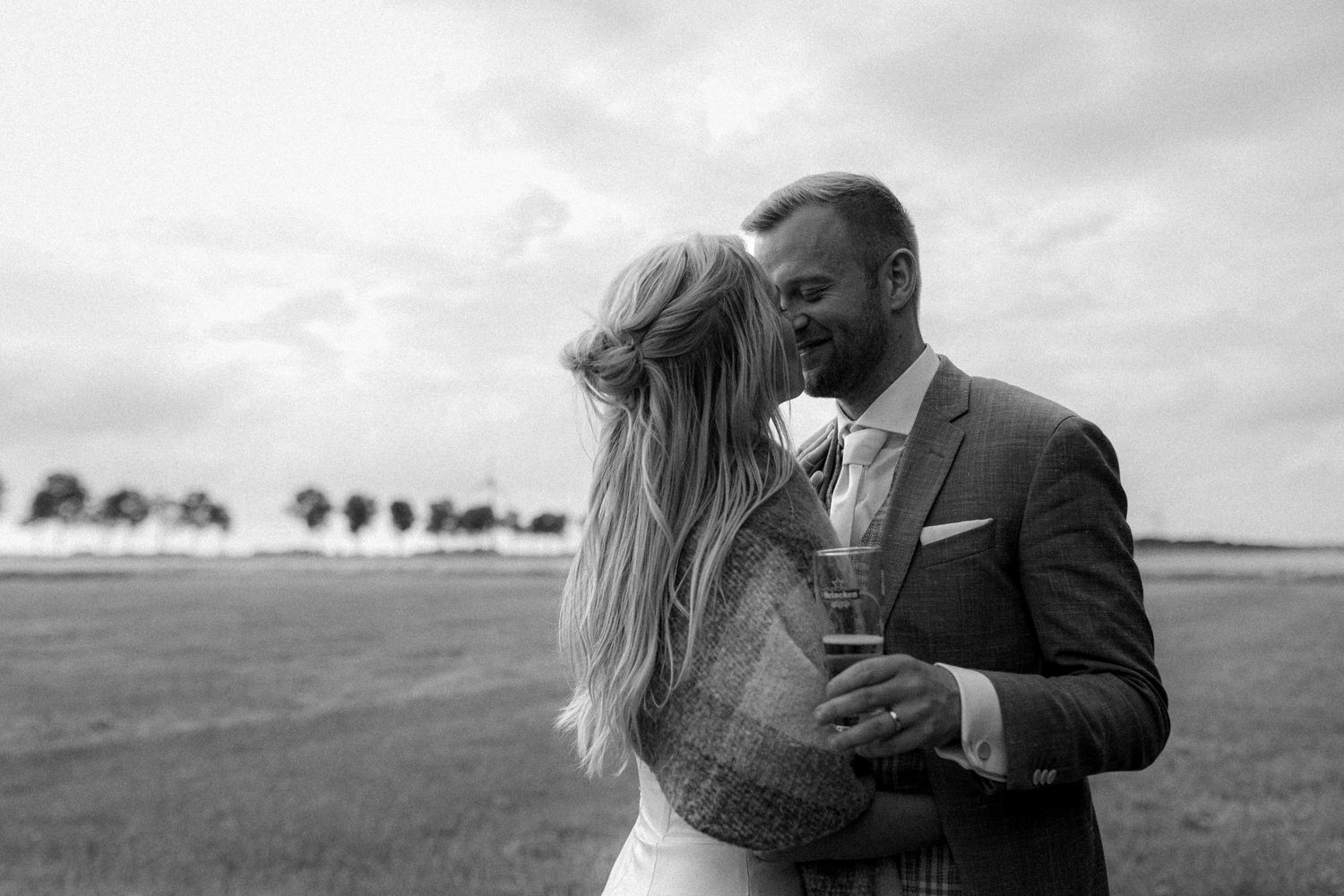 Romantic outdoor wedding photography session in a field with dramatic cloudy sky backdrop.